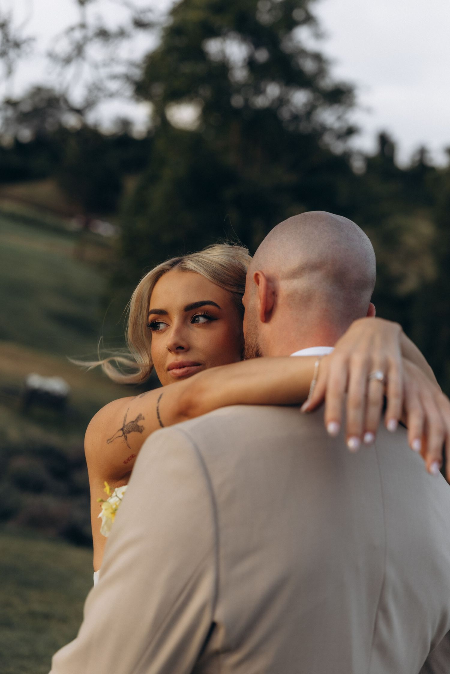 Intimate embrace between newlyweds in warm afternoon light on grassy hillside.