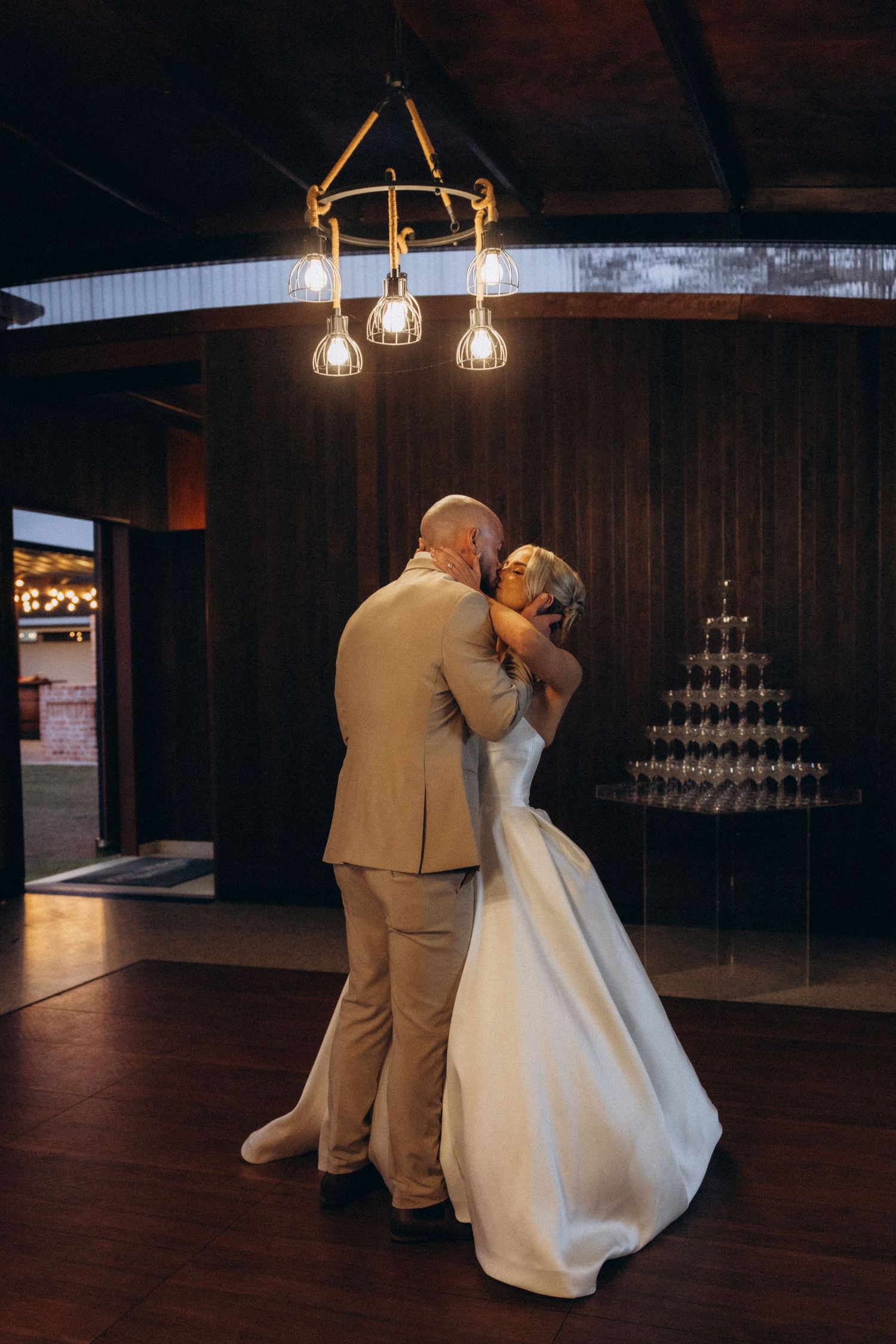 A couple shares an intimate dance moment in a dimly lit venue with wooden walls and hanging lights.