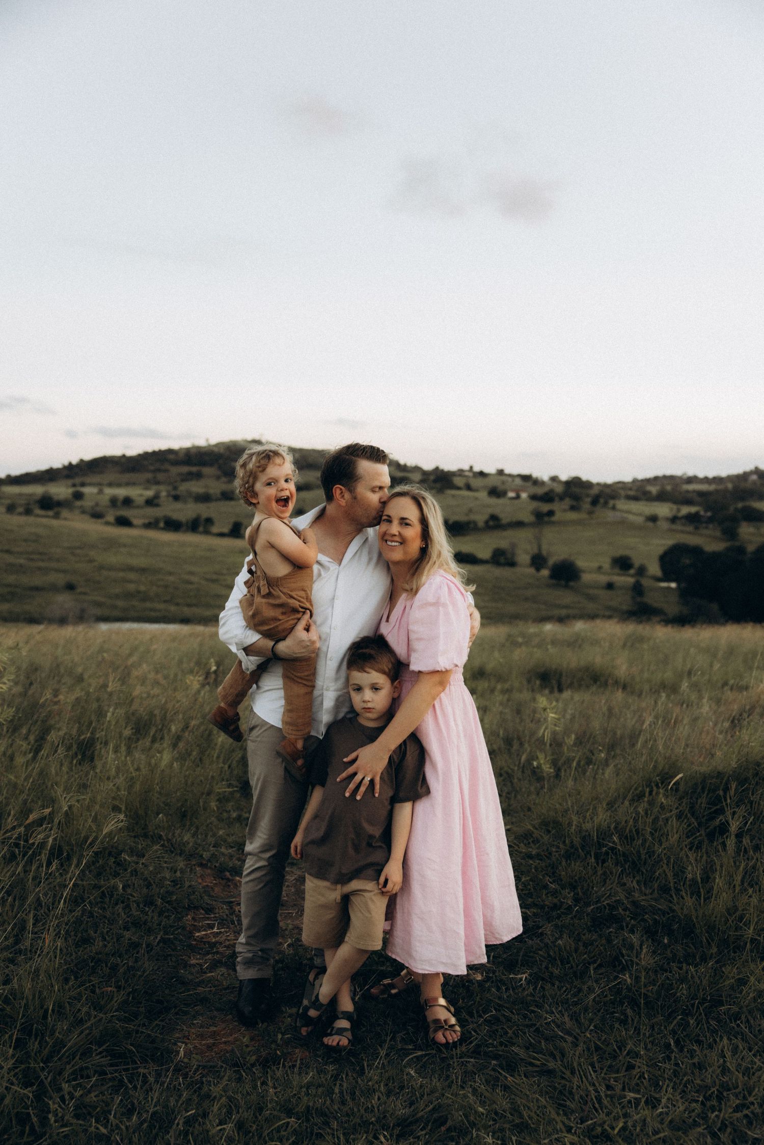 A family poses together in a beautiful countryside setting during sunset.