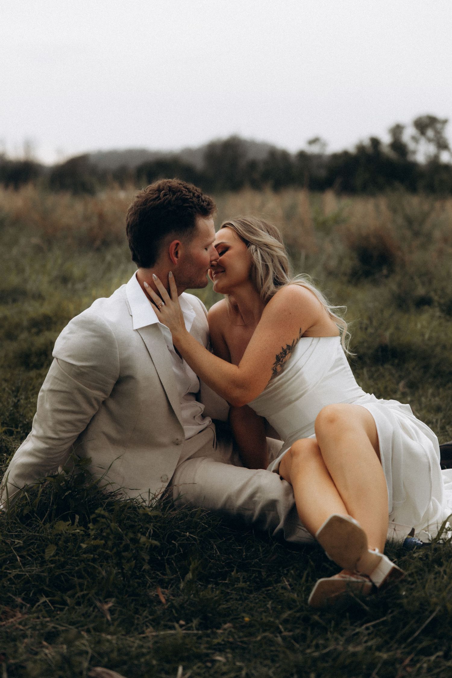 A romantic couple in white attire shares intimate moments while lying in a grassy field.