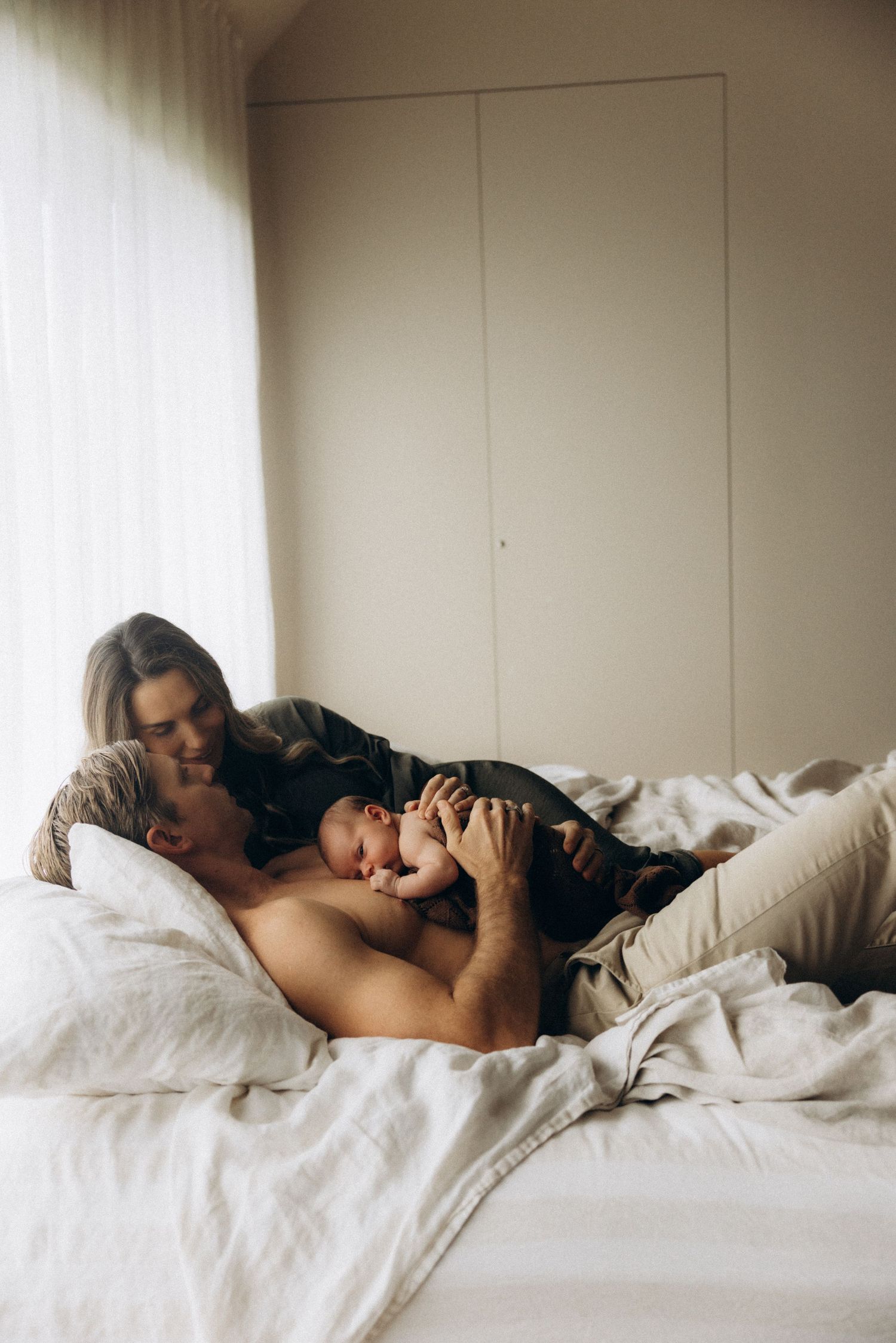Two people share a tender moment while resting on white bedding.
