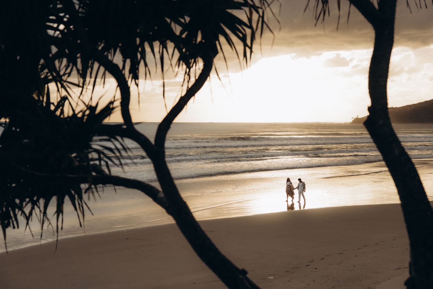 Silhouetted palm trees frame a beach scene at sunset.