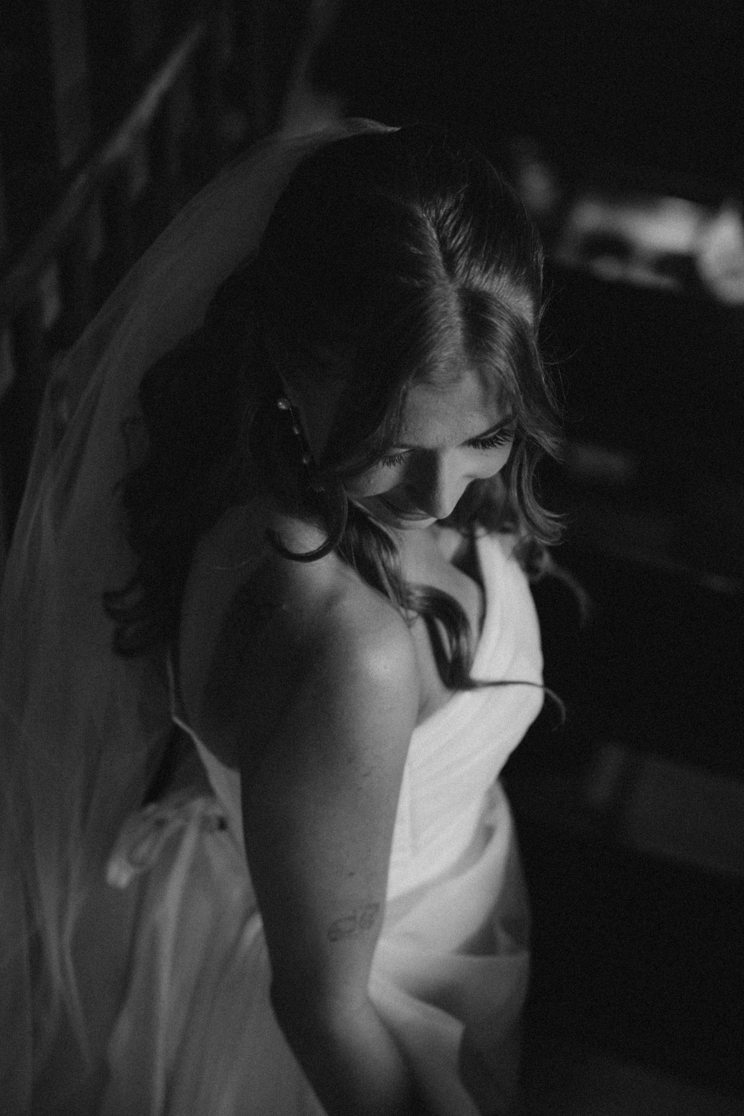 Black and white portrait of a bride in a wedding gown and veil in moody lighting.