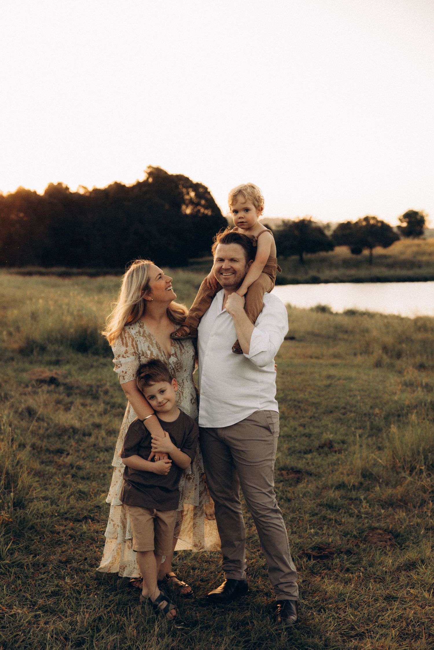 Family enjoying playful moments together in a golden-lit field at dusk.