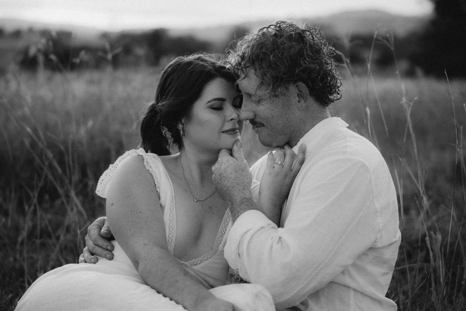 Black and white portrait of couple's tender embrace in natural setting.