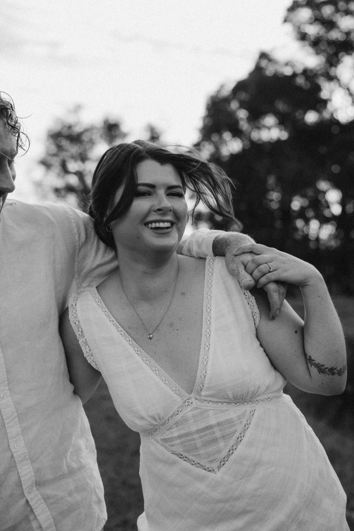 Candid black and white portrait of a bride laughing in a lace-trimmed dress.