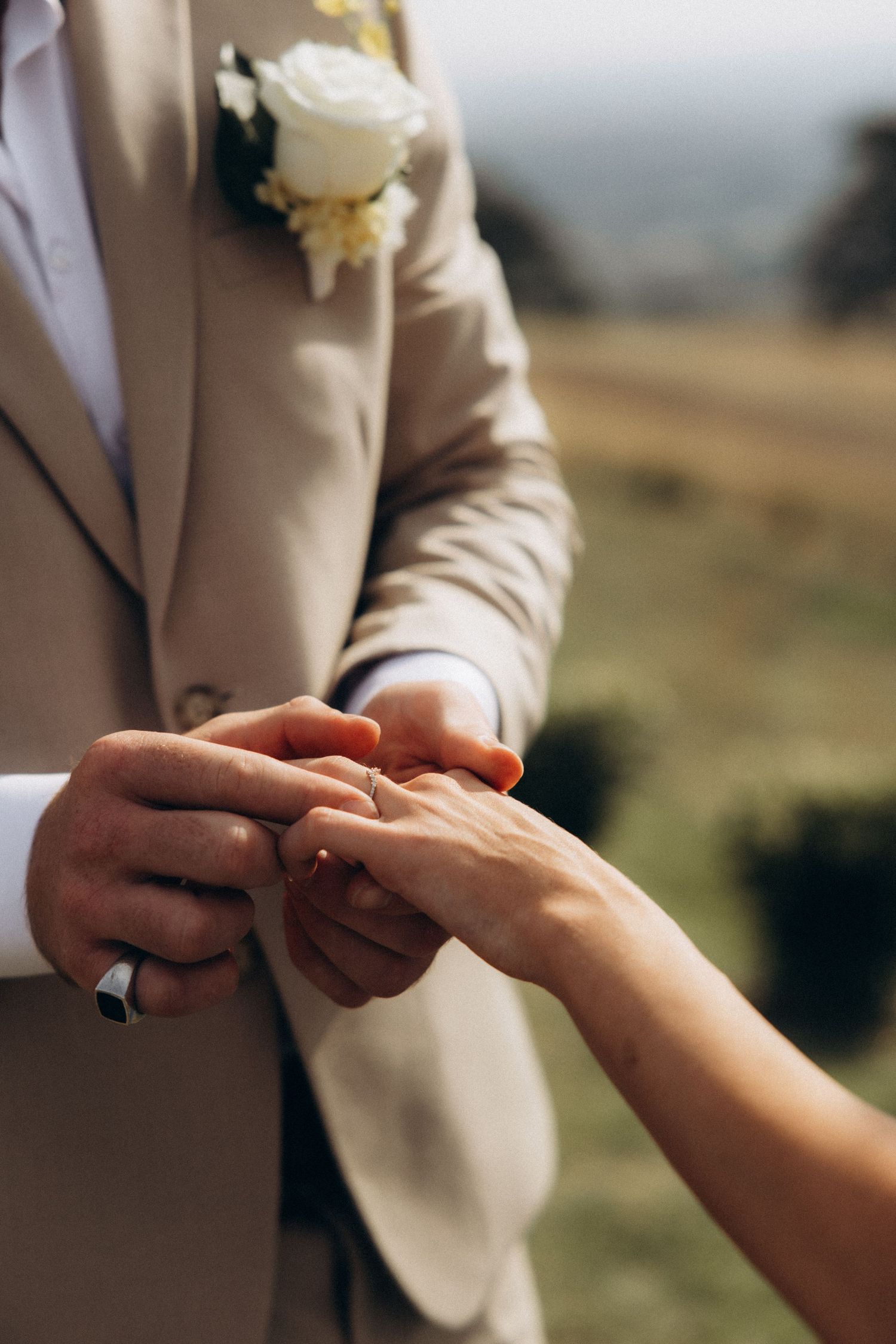 Close-up shots of hands exchanging rings during outdoor wedding ceremony.