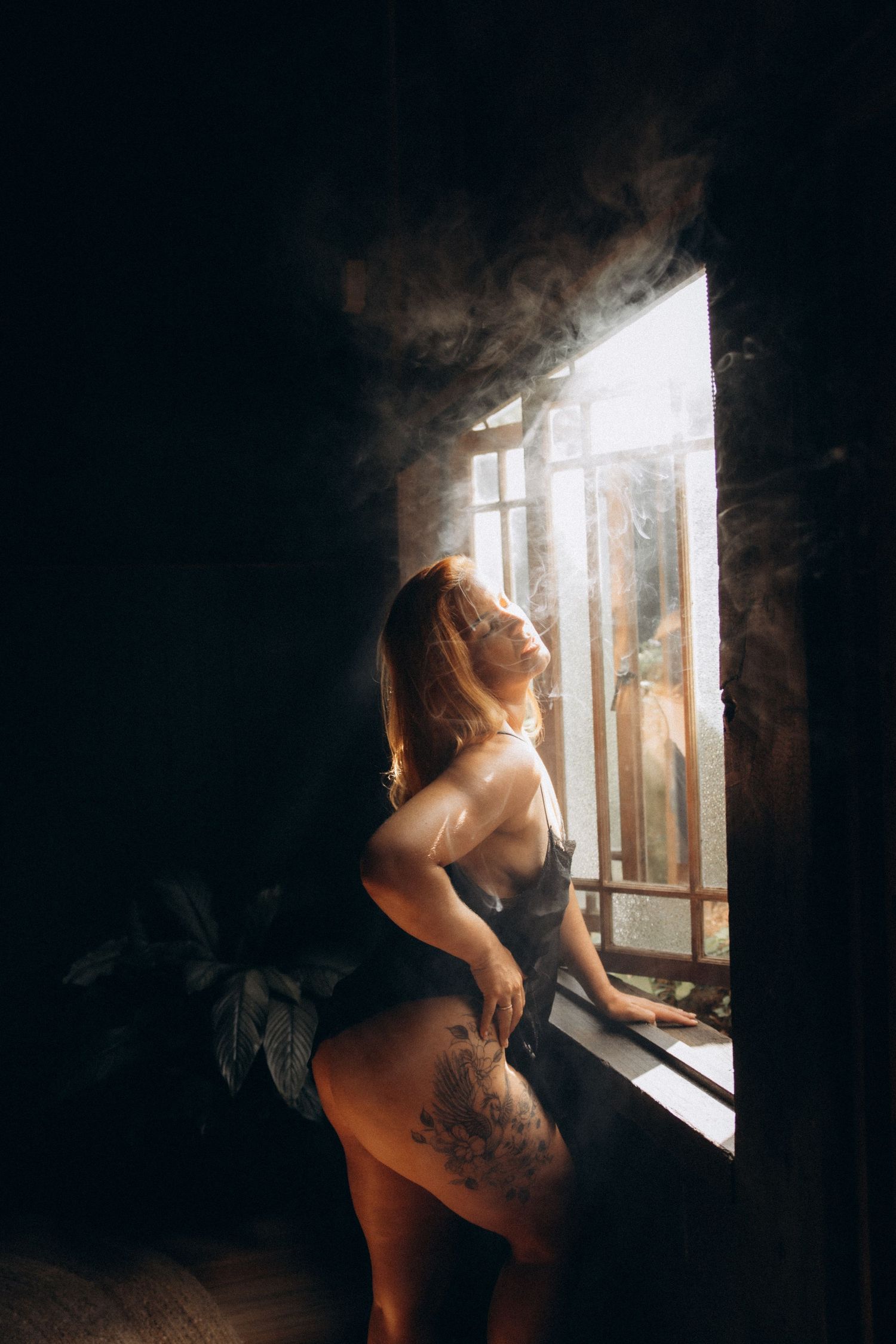 Artistic maternity photo by window with dramatic natural lighting and shadows.