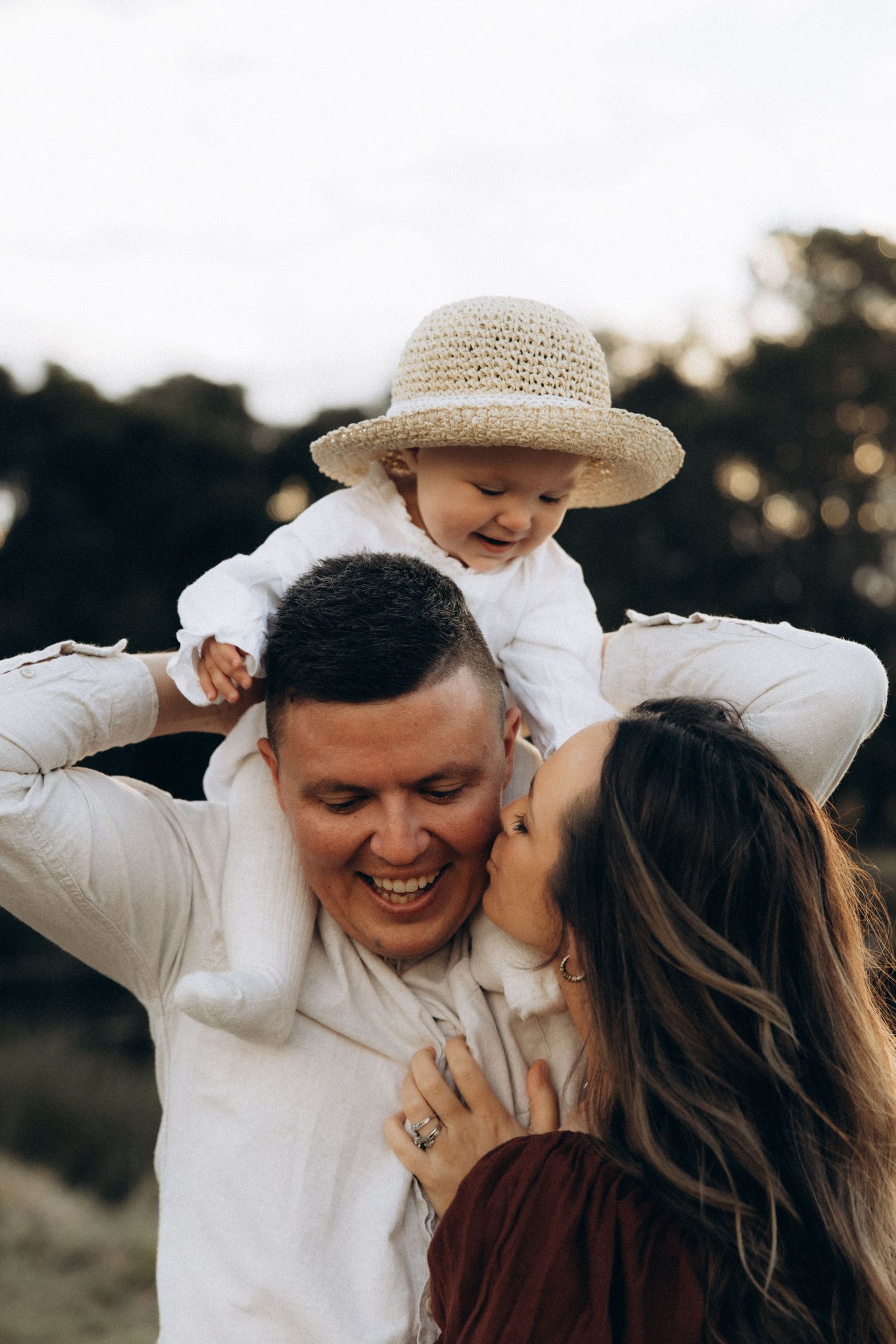 Playful family moment outdoors with straw hat and natural lighting.