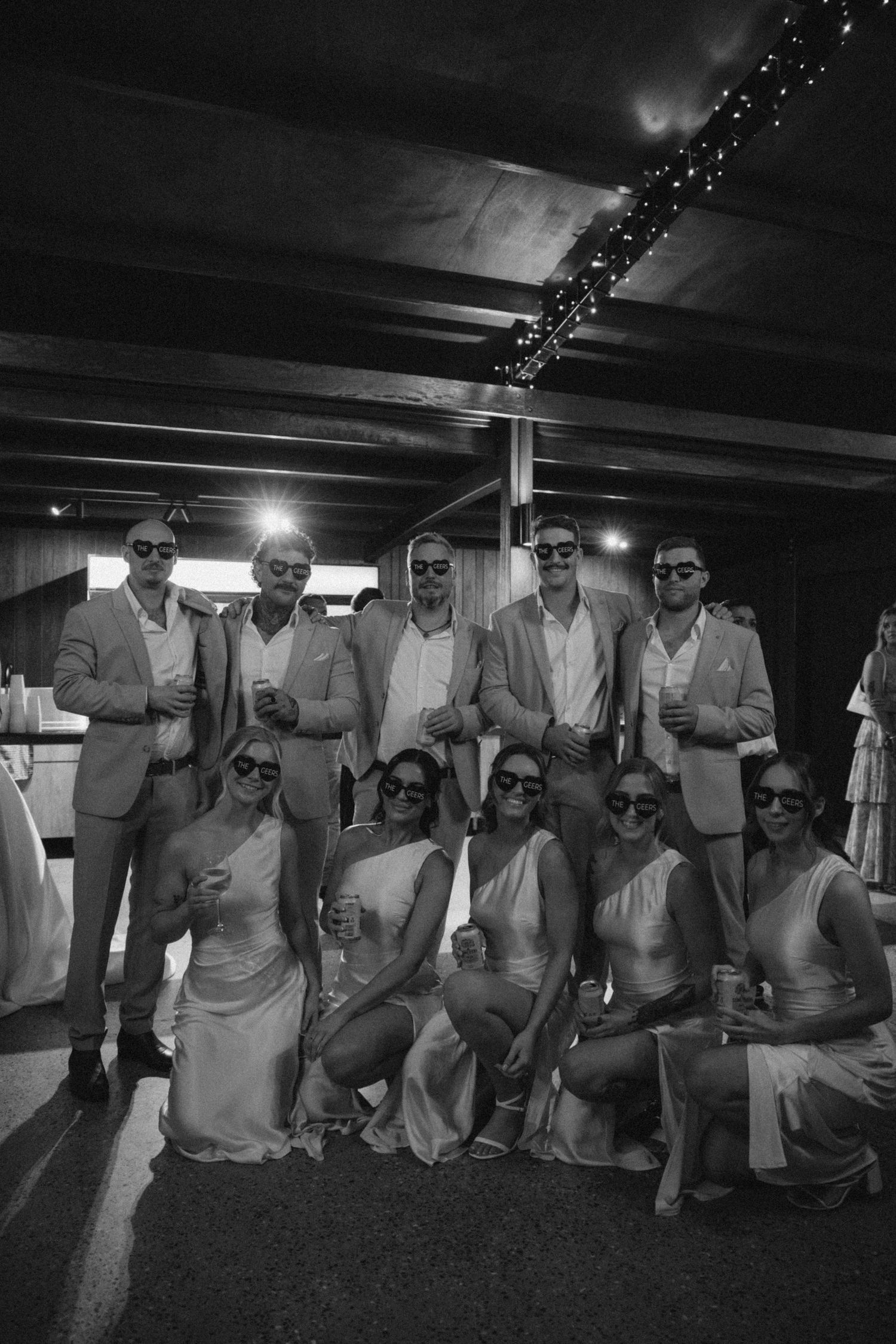 Wedding party members in light colored suits and sunglasses pose for a group photo.