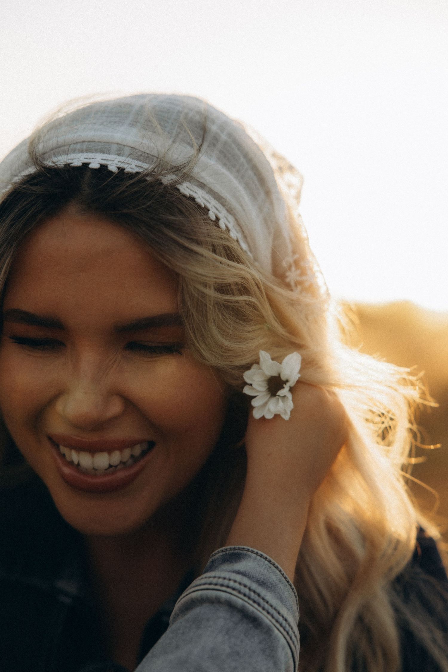 Person with blonde hair and white flowers smiling in warm sunlight.