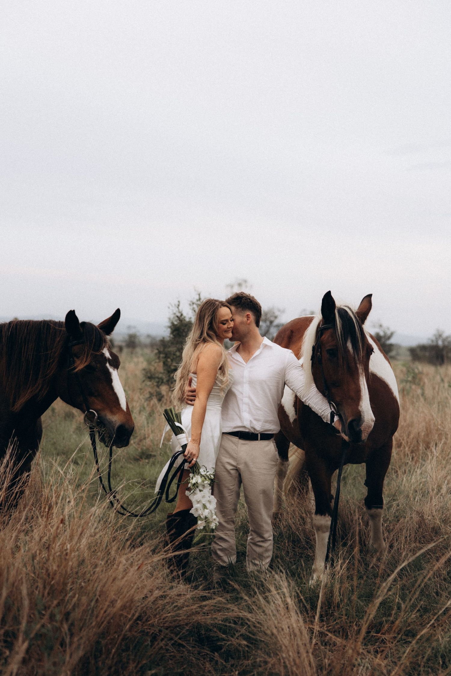 Romantic countryside photoshoot with horses in tall grass.