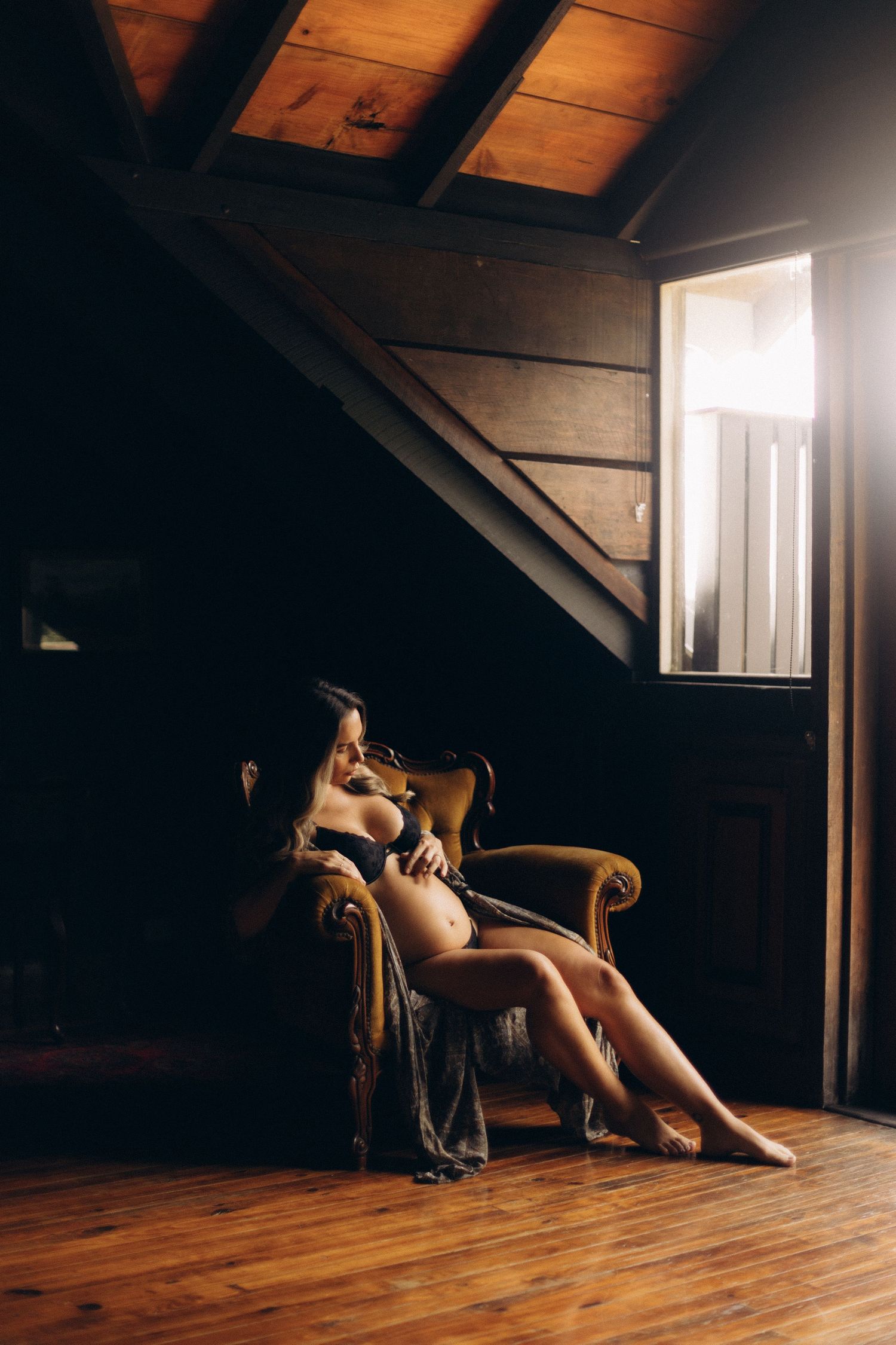 Moody interior scene with sunlight streaming through attic window onto wooden floor.