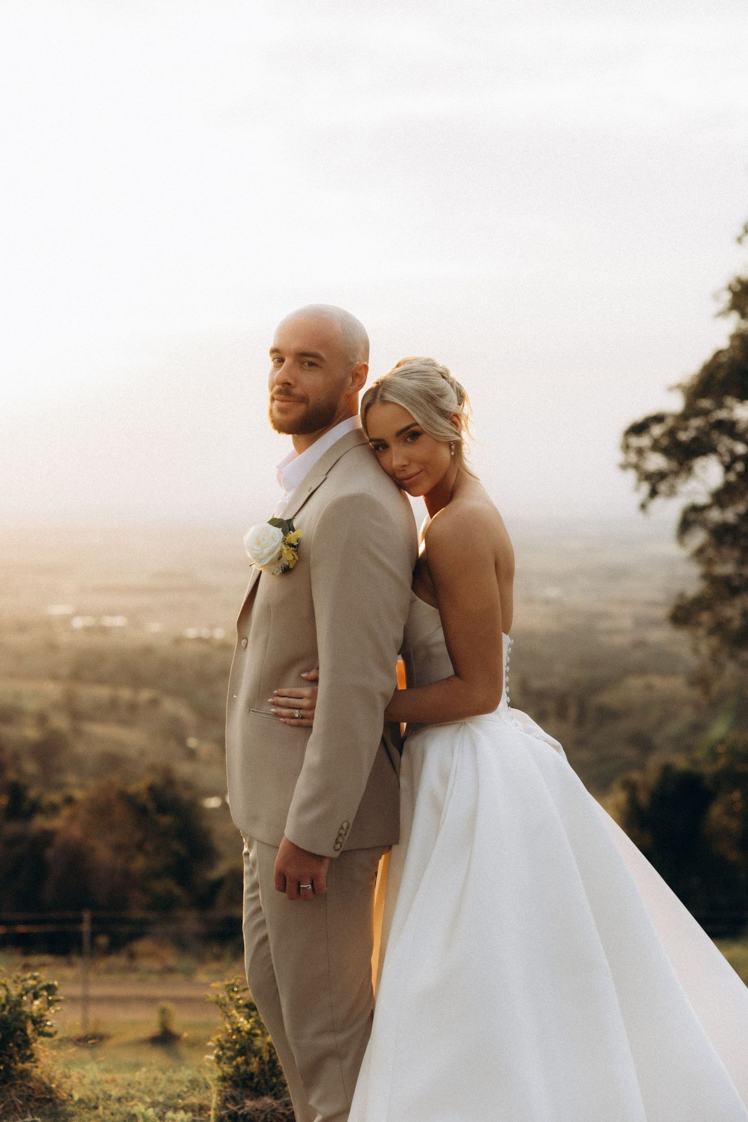 A couple embracing on a hilltop overlooking a scenic valley at sunset.
