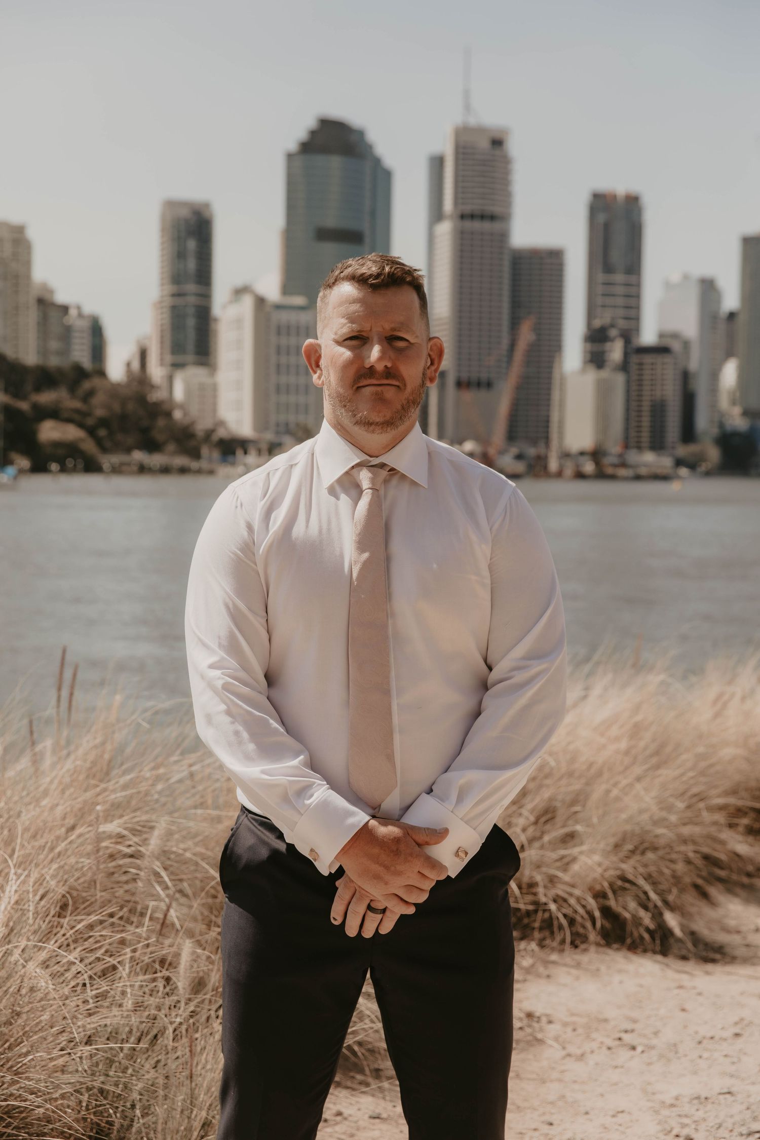Man in white dress shirt and tie poses against city skyline backdrop with tall buildings.