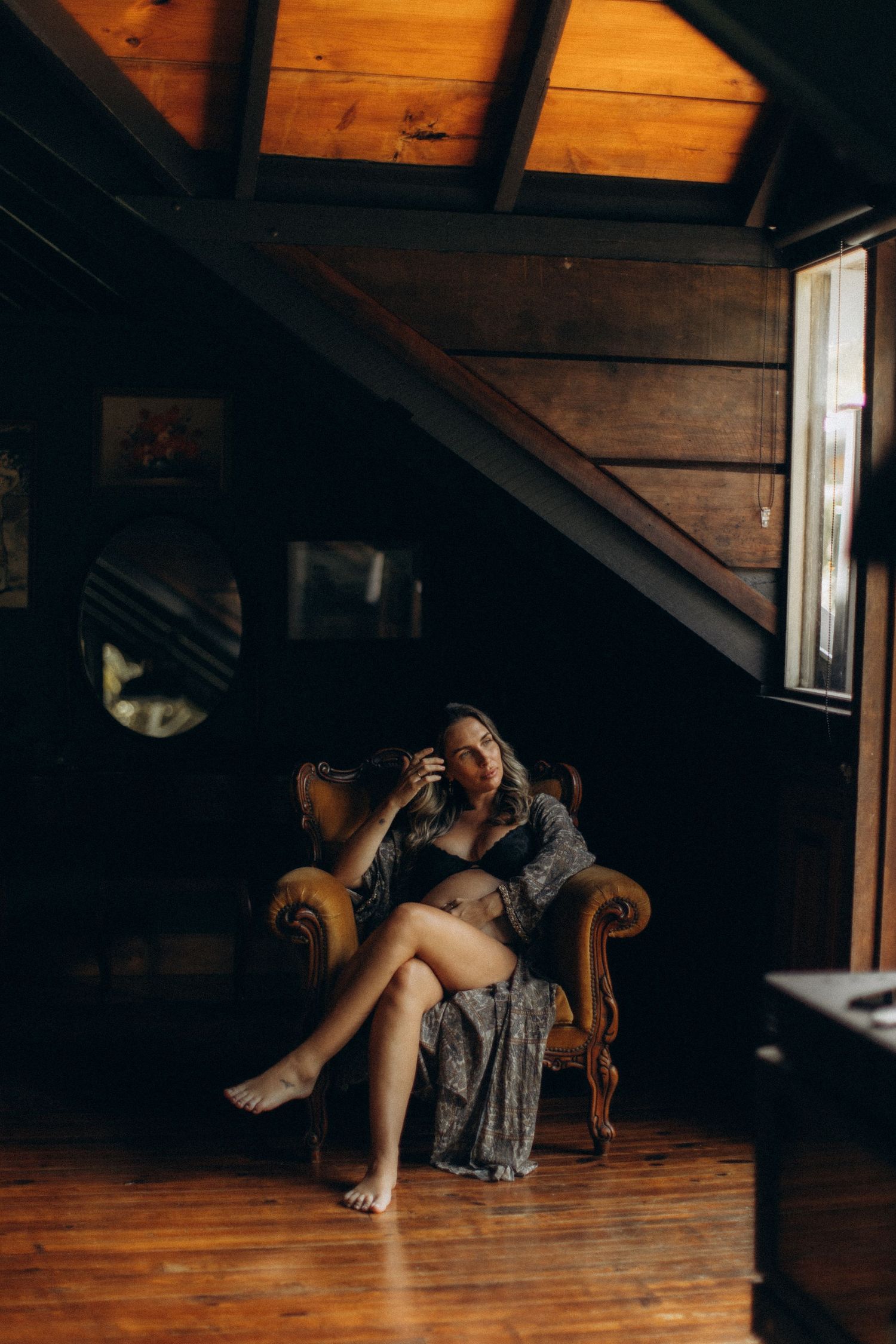 A moody boudoir scene in a rustic cabin attic with warm wood tones and a vintage velvet armchair.