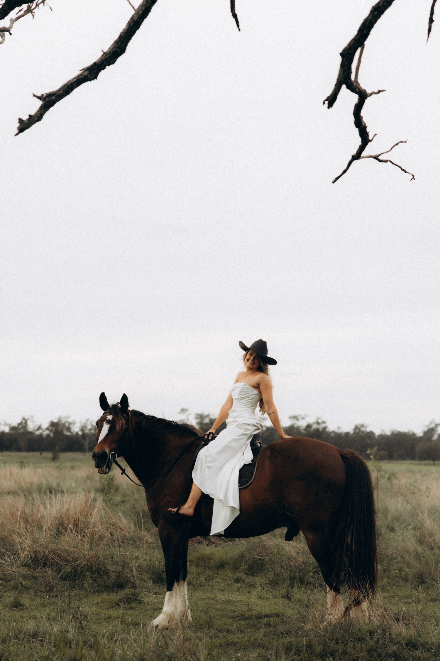 A person in white clothing rides gracefully on a dark draft horse in a meadow.