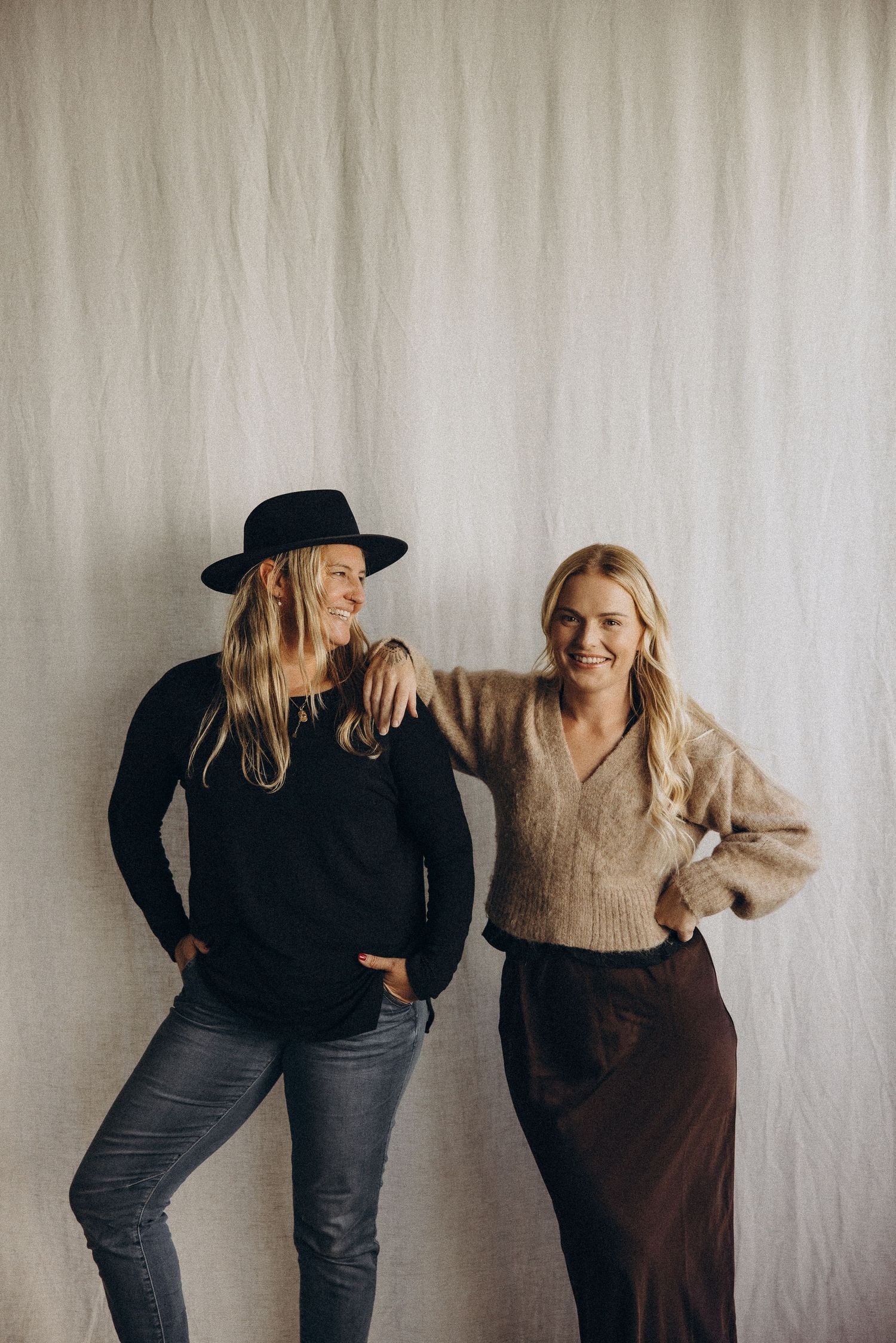 Two friends posing playfully against a white backdrop in casual winter outfits.