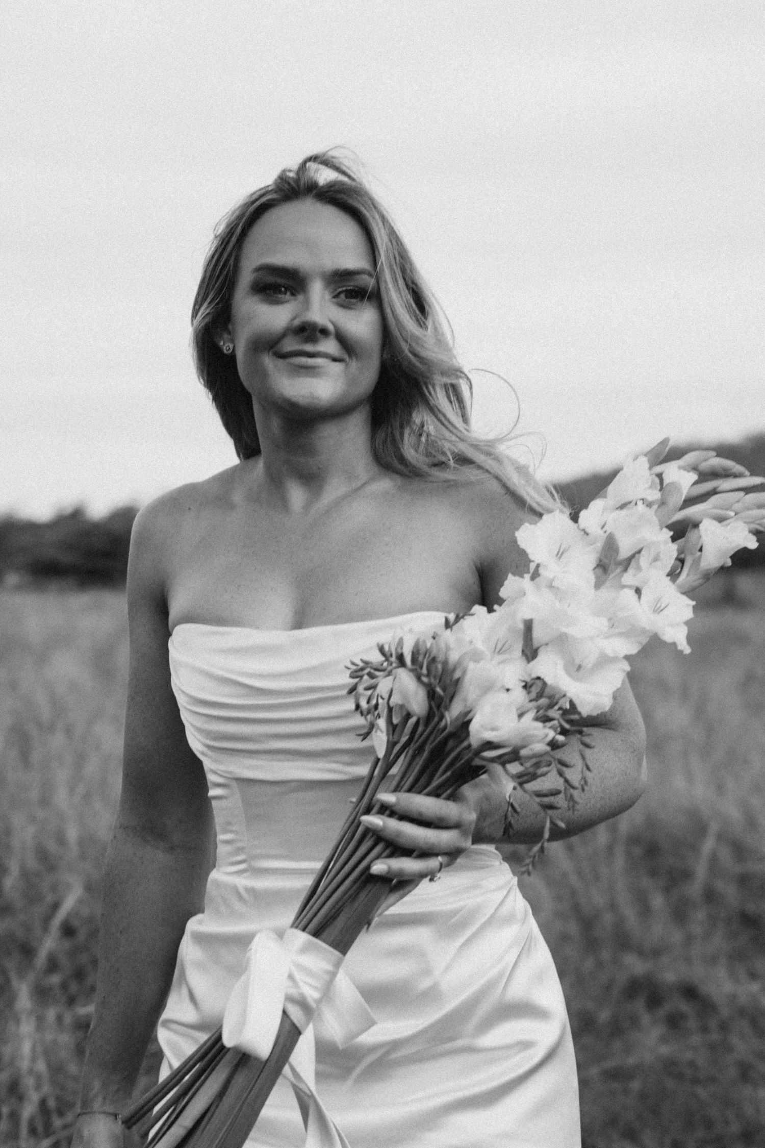 A bride holds a bouquet of white flowers in a strapless wedding dress.