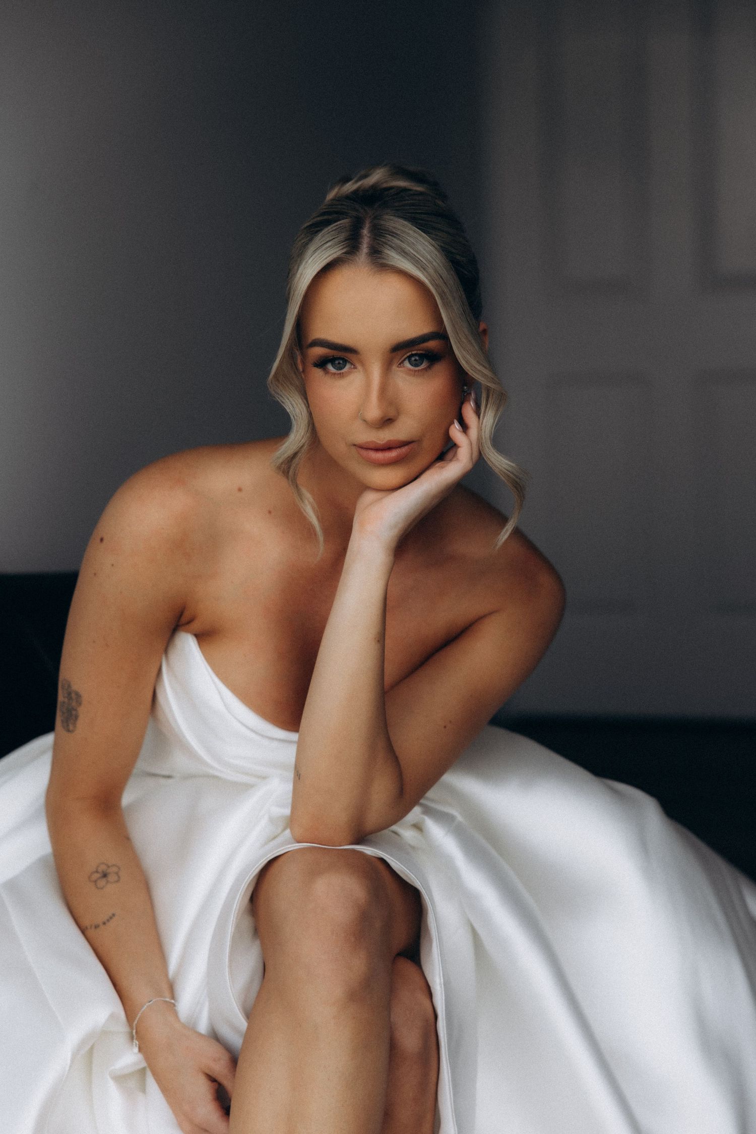 Bride in white gown poses elegantly against dark background during wedding preparations.