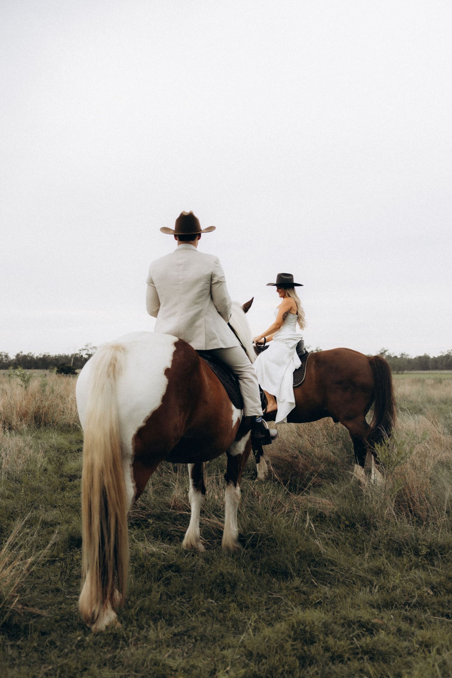 Two people on horseback ride together through a peaceful meadow landscape.