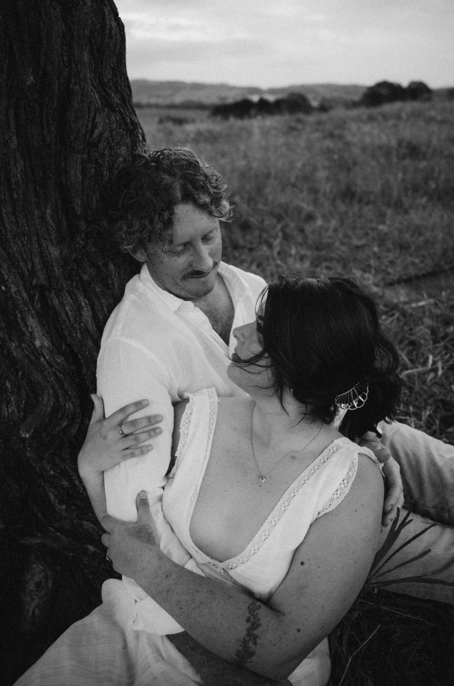 An intimate black and white portrait of a couple sharing a tender moment under a tree.