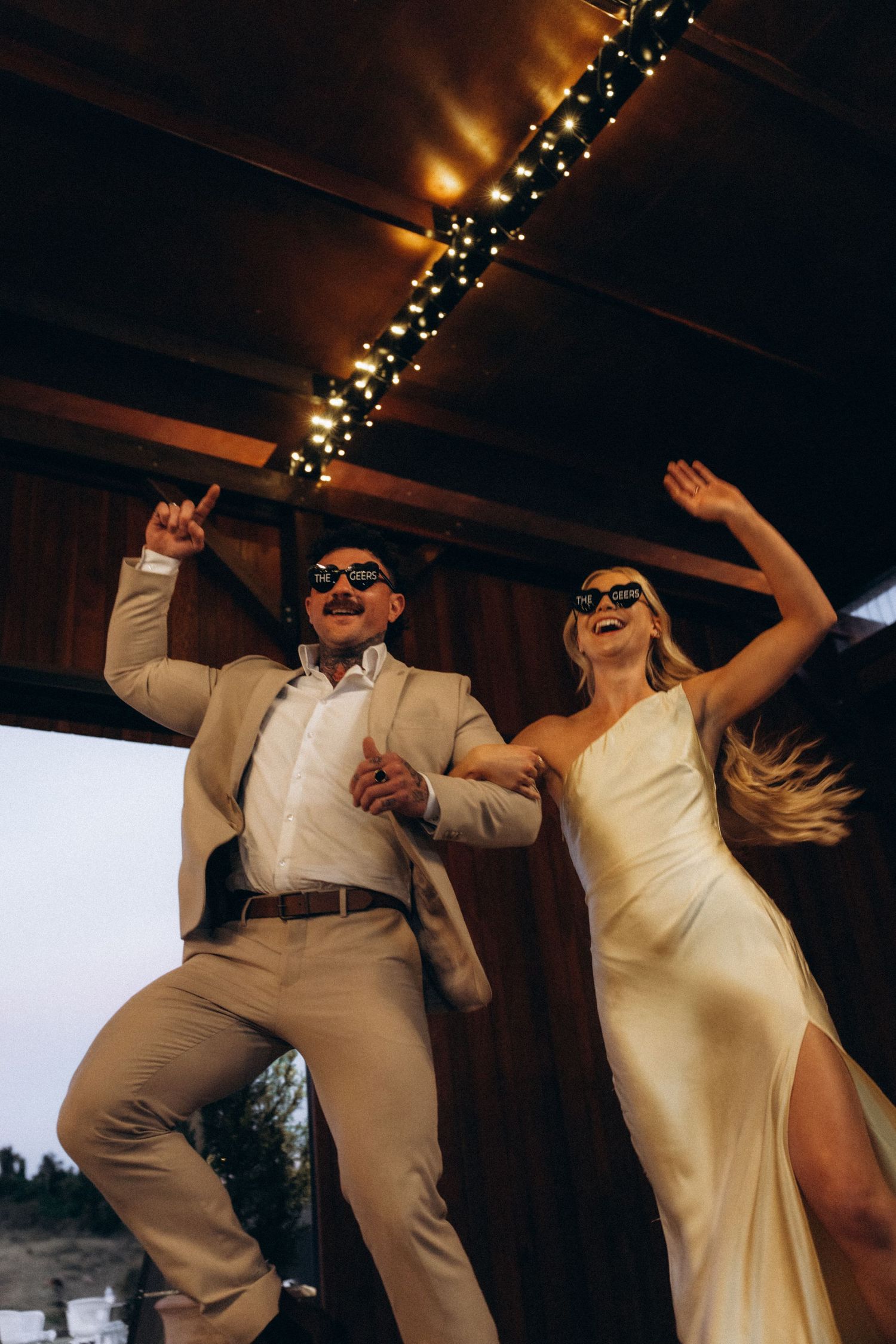 Wedding party members dancing and celebrating in formal attire under string lights.