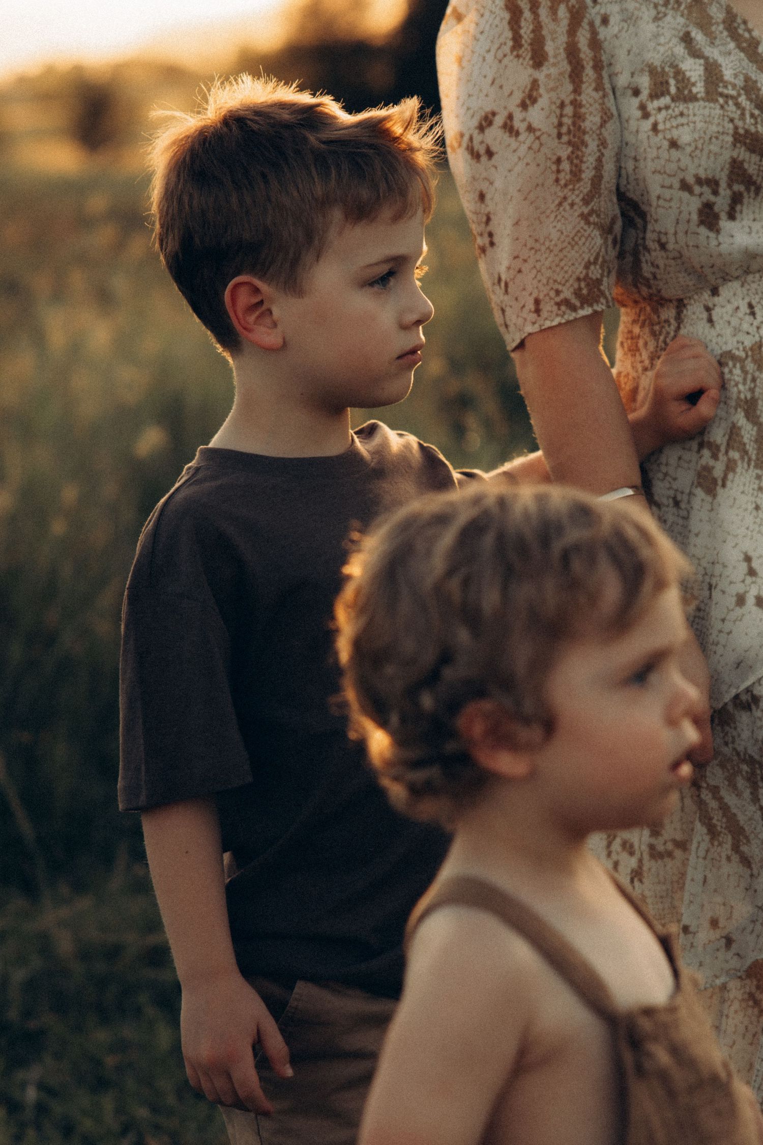 Two children stand close together near a tree trunk in warm sunset lighting.