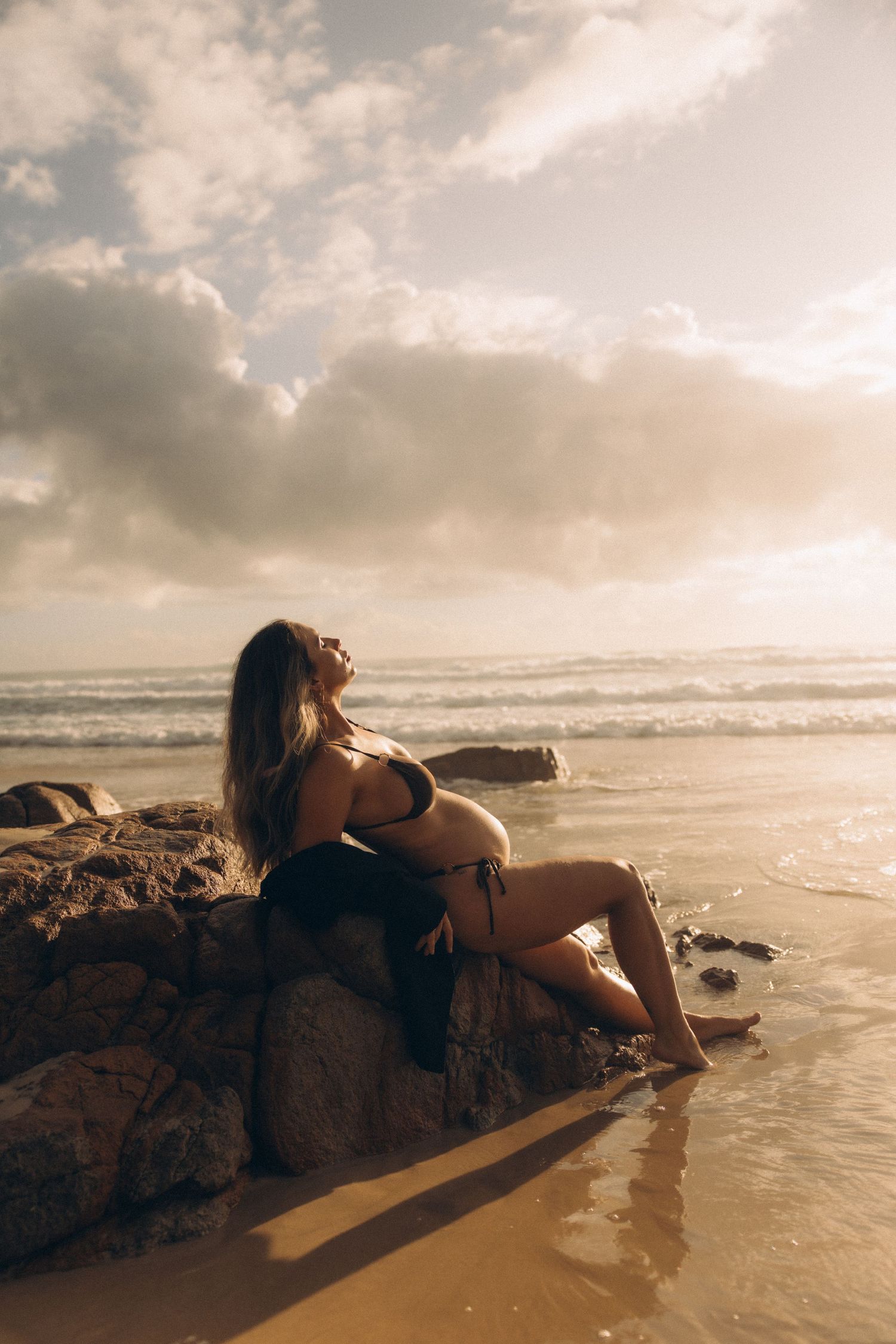 Sunset beach portrait on rocky shore with golden light and ocean waves.