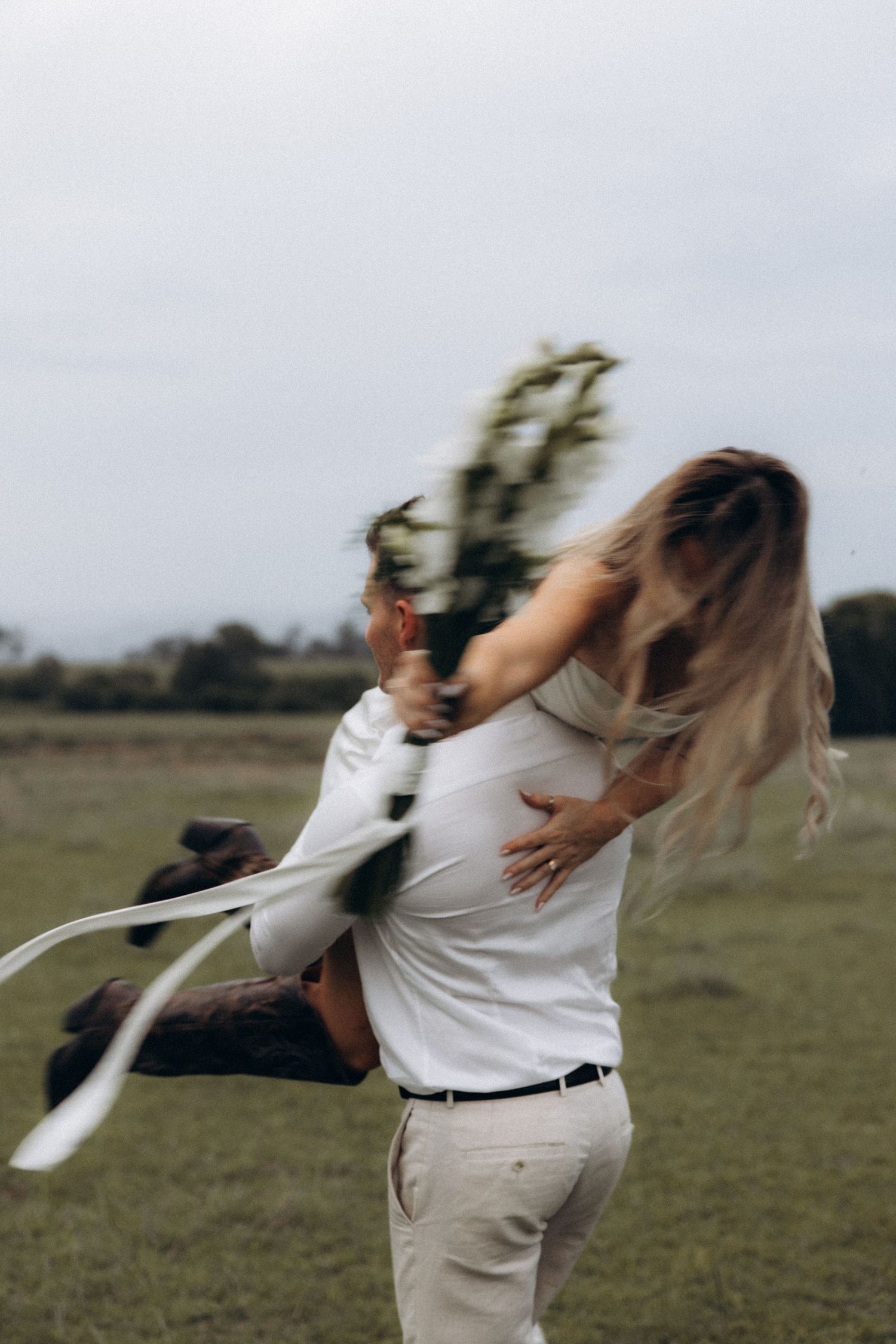 A couple dancing and twirling in a field on an overcast day.