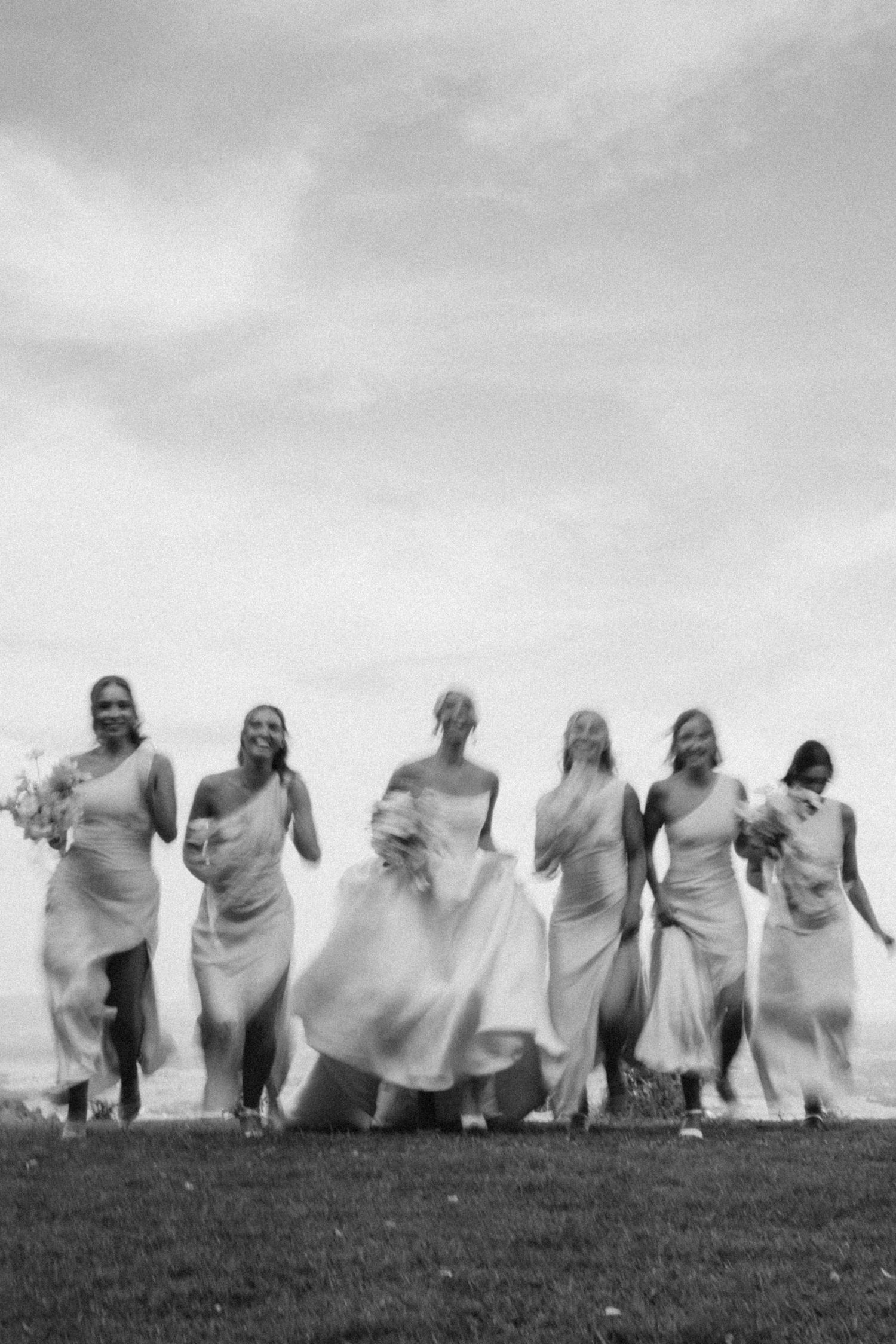 Black and white photo of bridal party running joyfully across a hill.