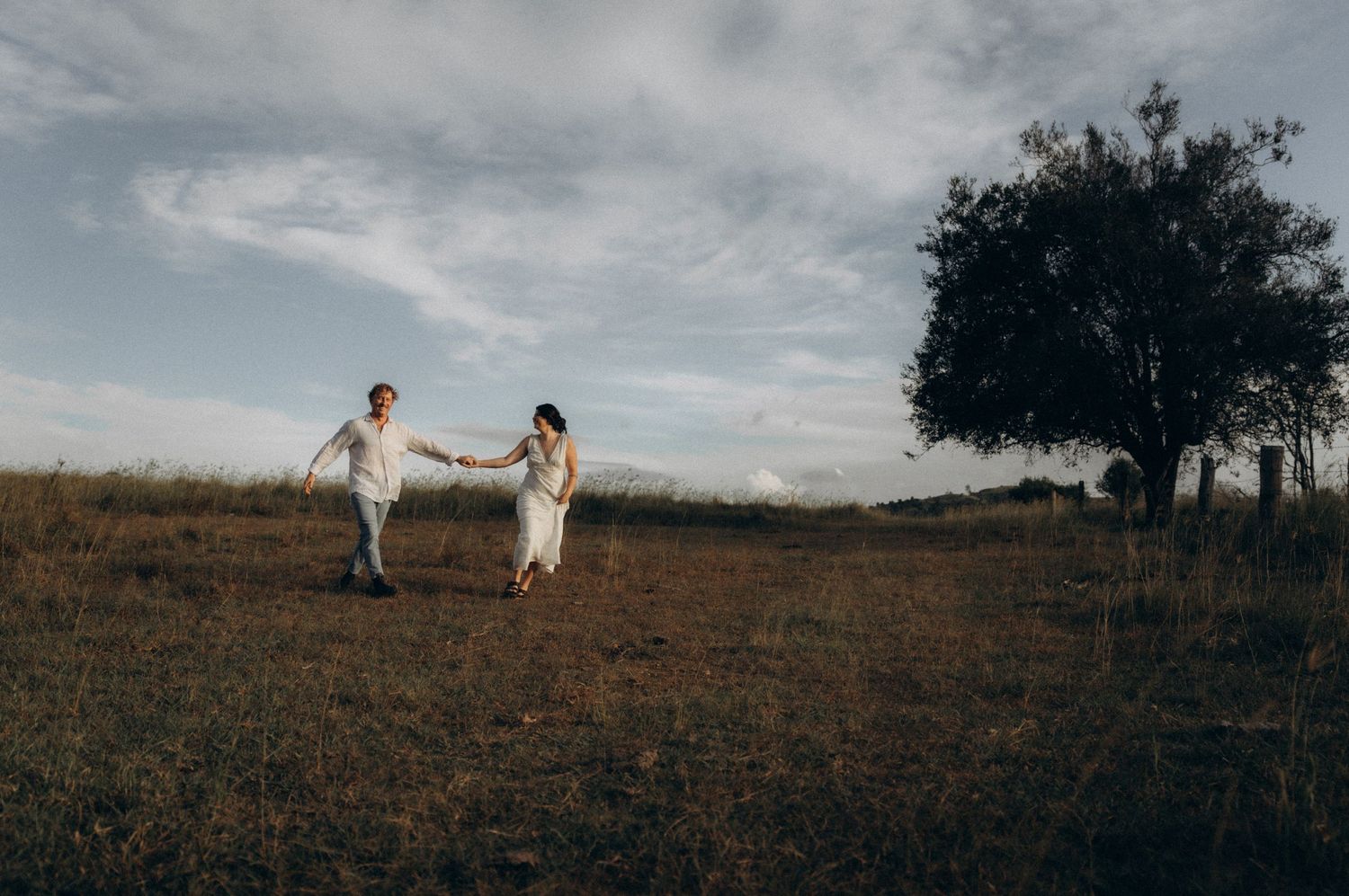 A romantic couple's photoshoot in a wide open field with dramatic clouds overhead.