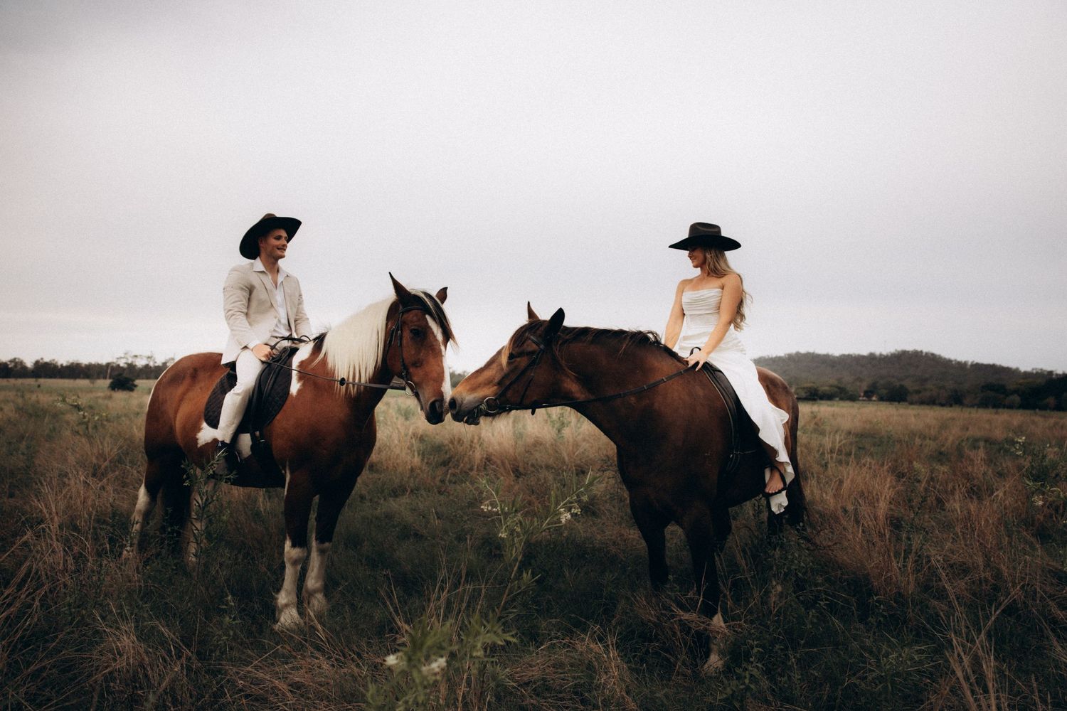 Wide panoramic view of horses and riders in a grassy field.