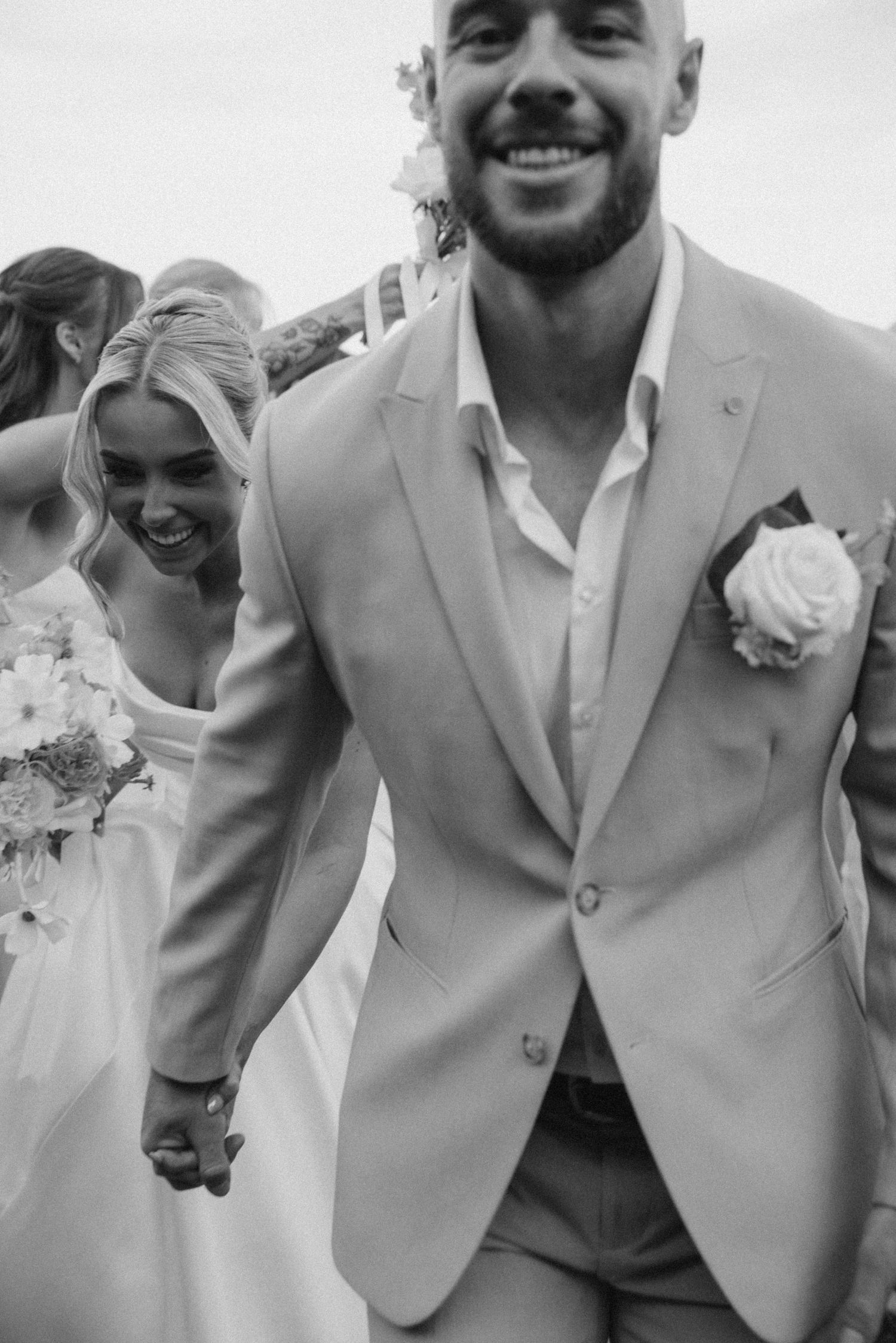 Black and white candid photo of couple sharing joyful moment at outdoor wedding.