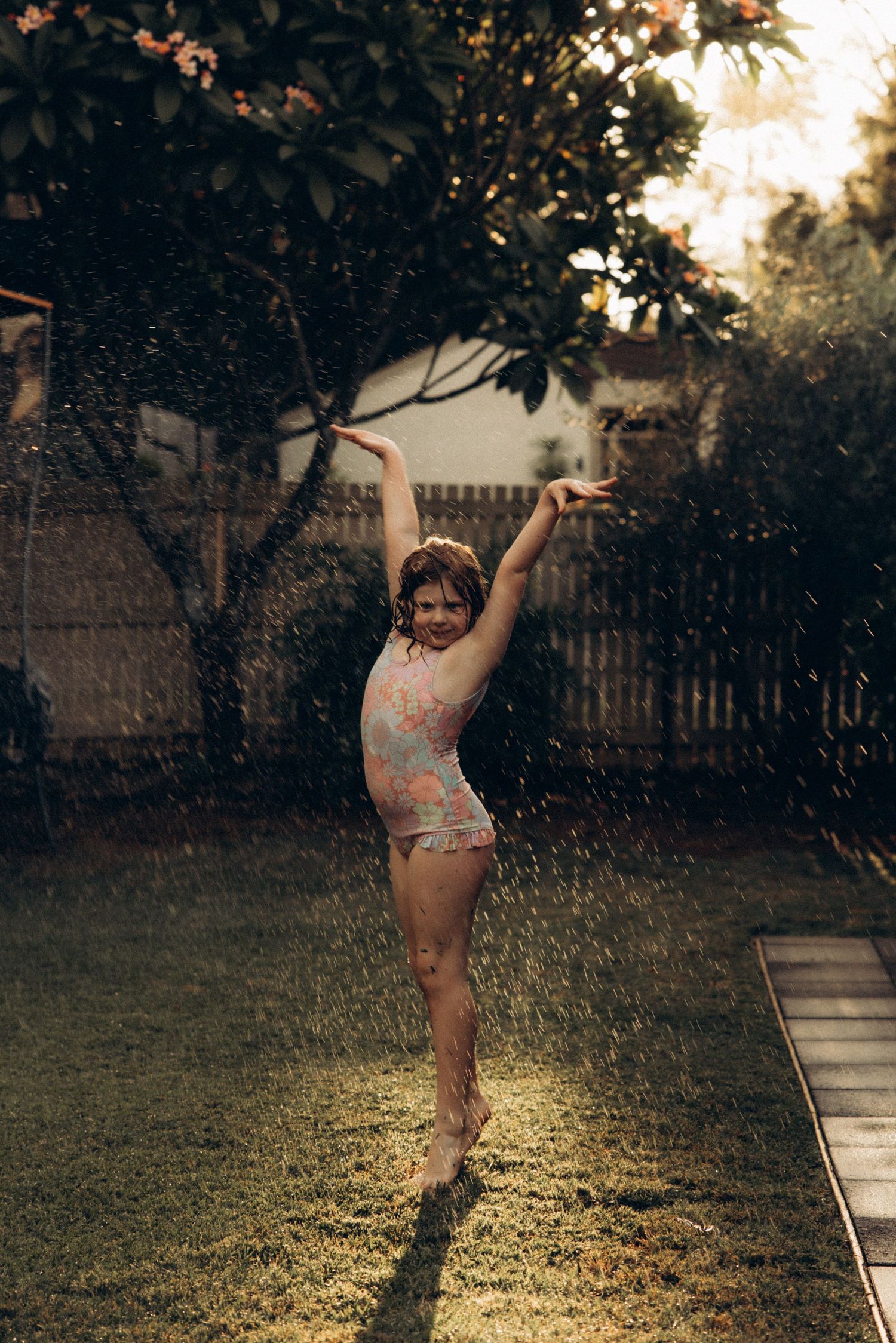 Young child playing in sprinkler water on sunny day in backyard garden.