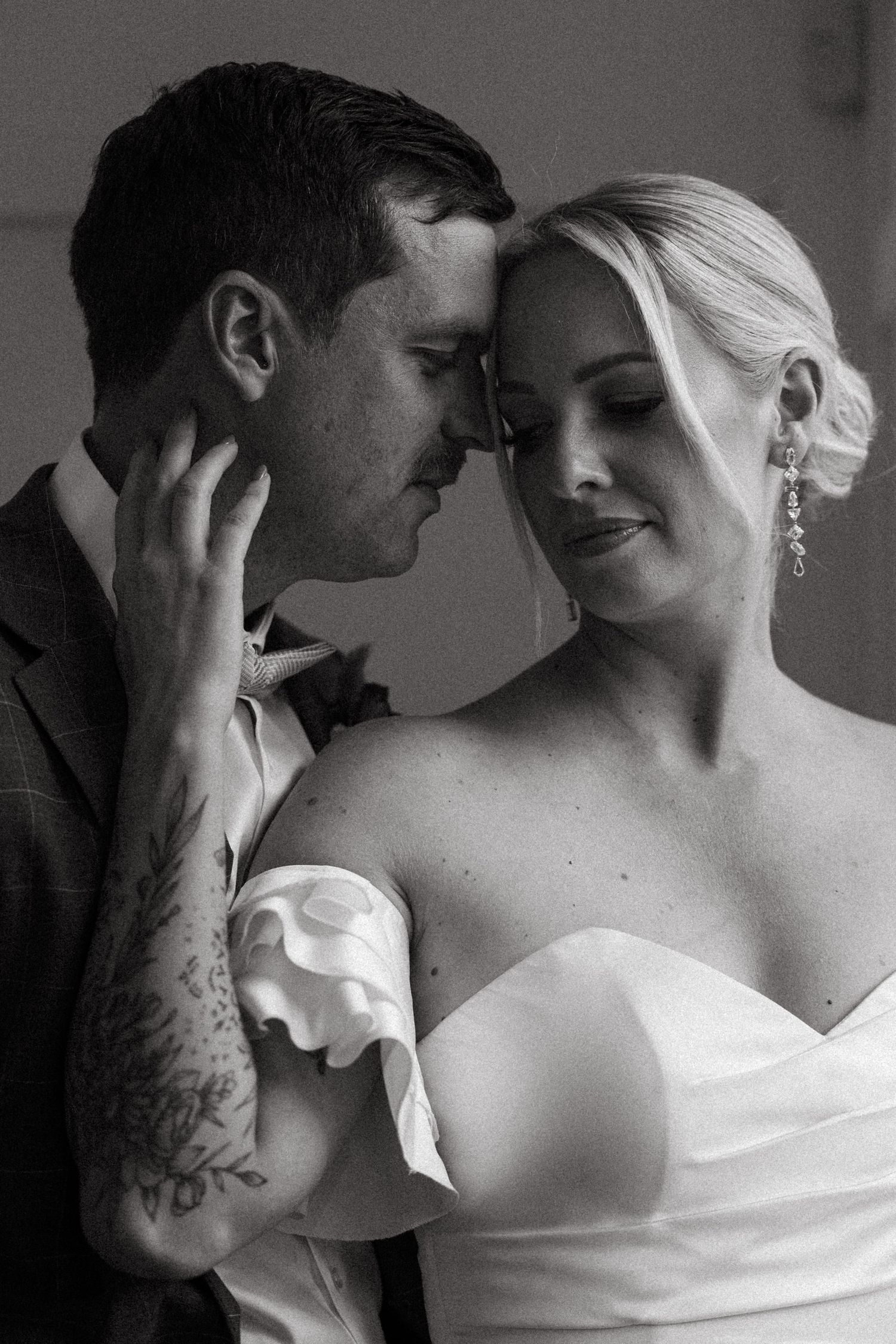 Intimate black and white portrait of couple in wedding attire sharing tender moment.