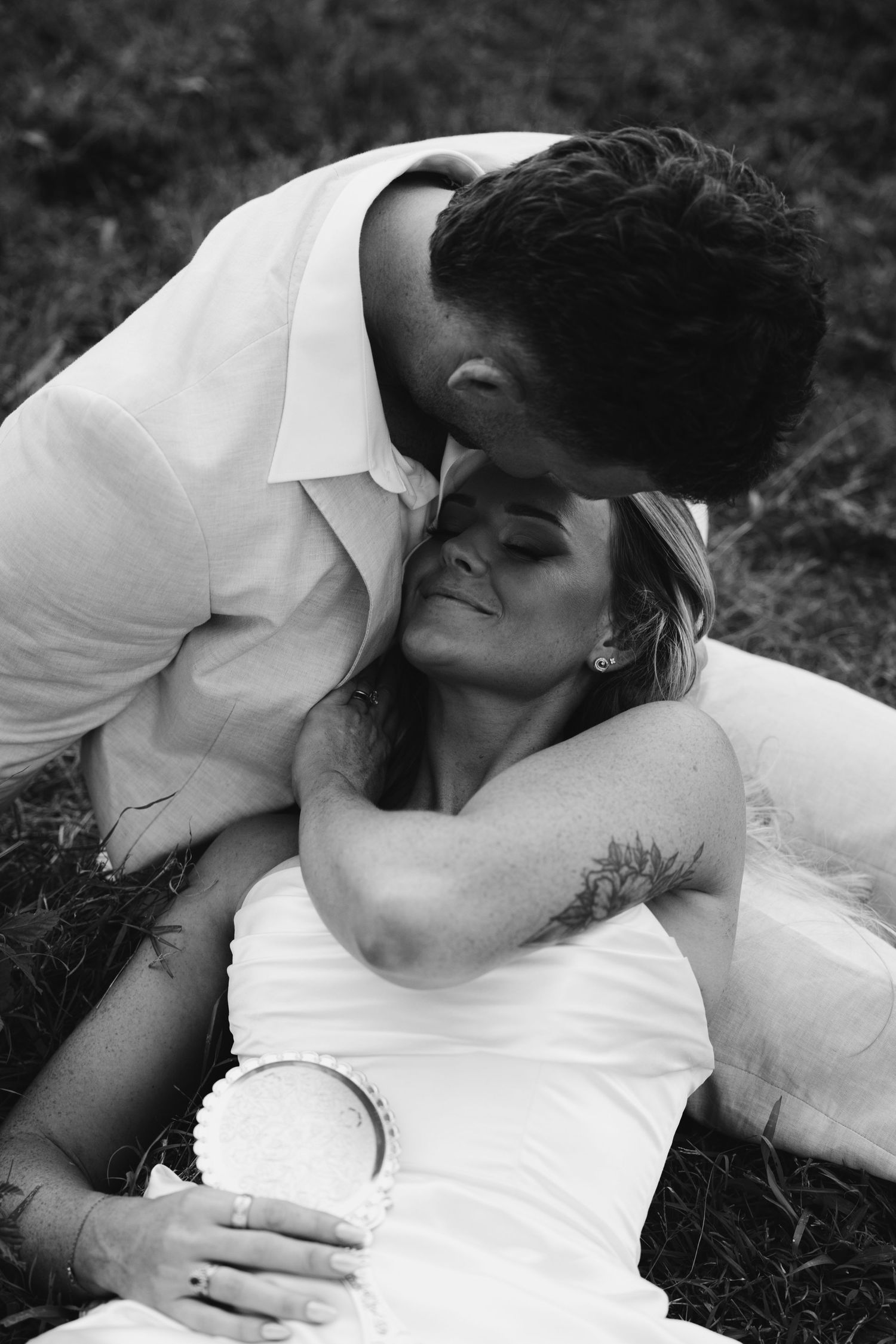 Intimate black and white photos of a couple in white clothing embracing on the ground.