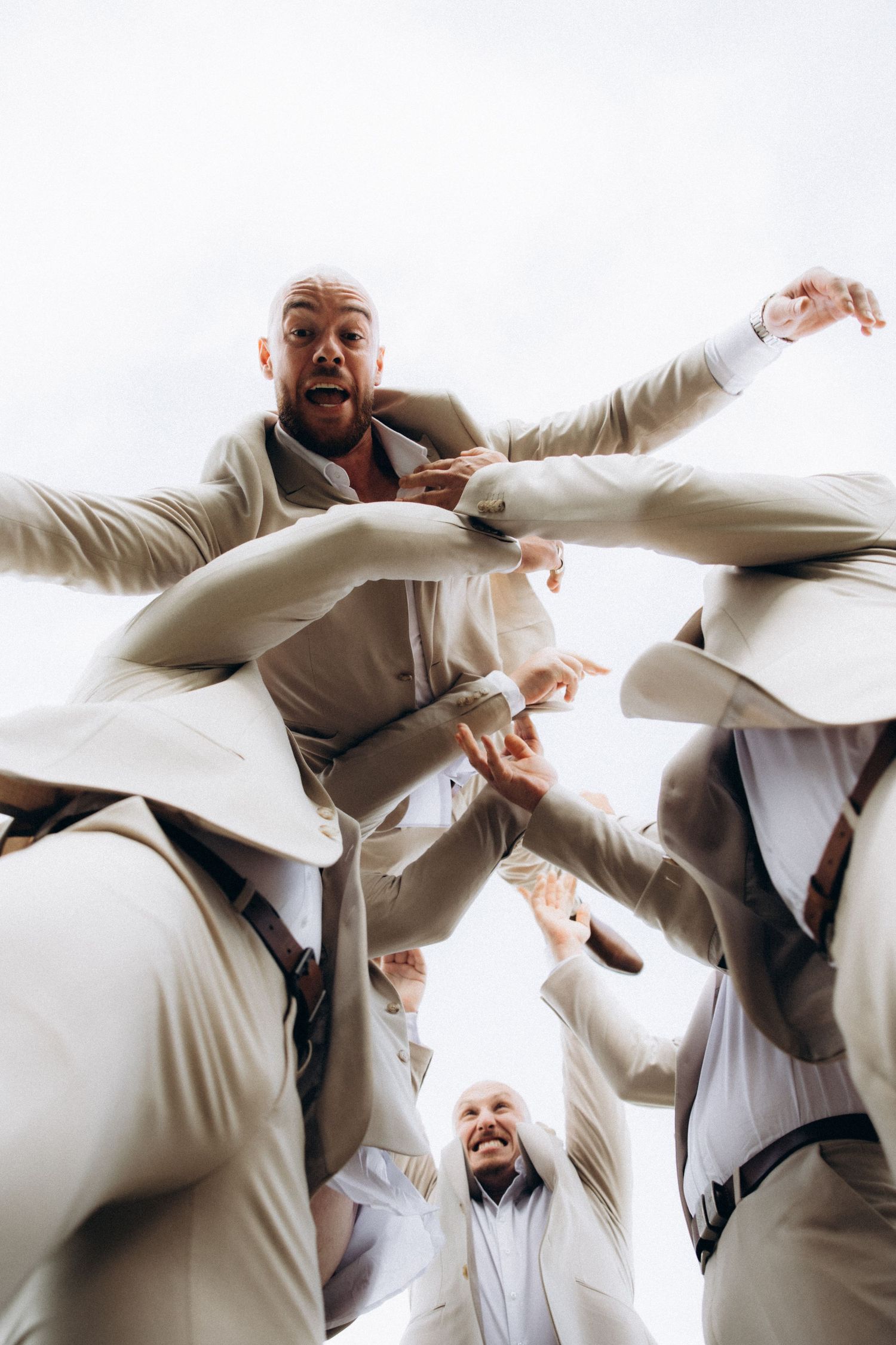 Groomsmen in light suits huddle together for fun low-angle photo.