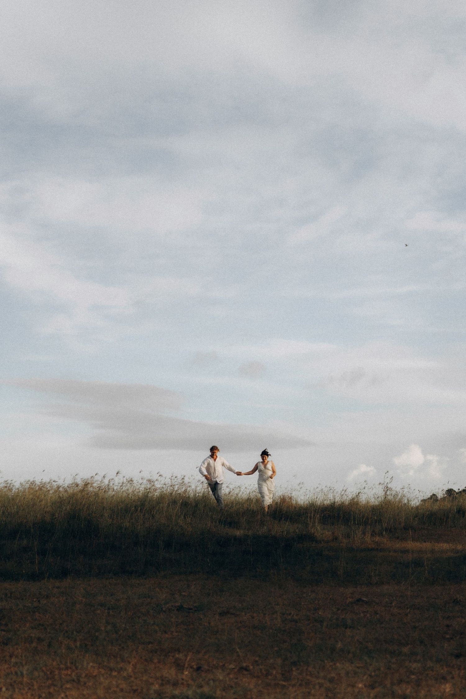Silhouettes of two people standing on a hill against a cloudy sky.