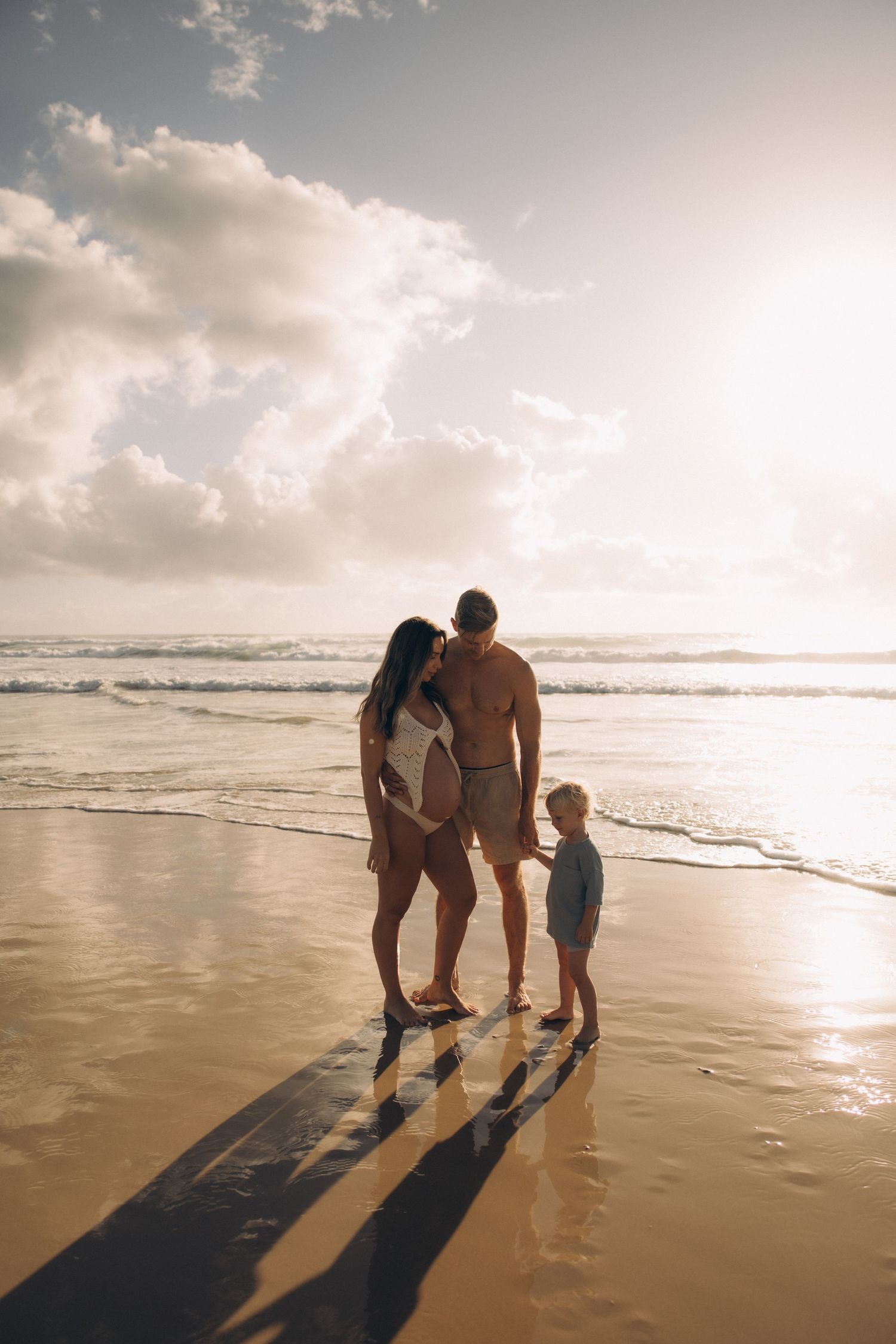Three silhouettes walk along a beach shoreline during golden hour with waves crashing nearby.