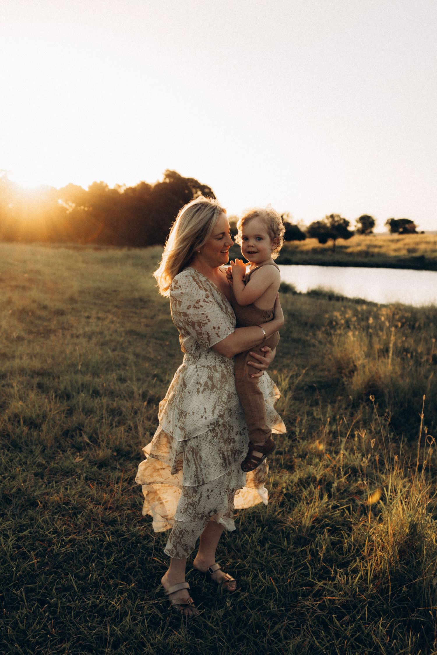 Children play together in a grassy field during golden hour with sunlit trees in the background.