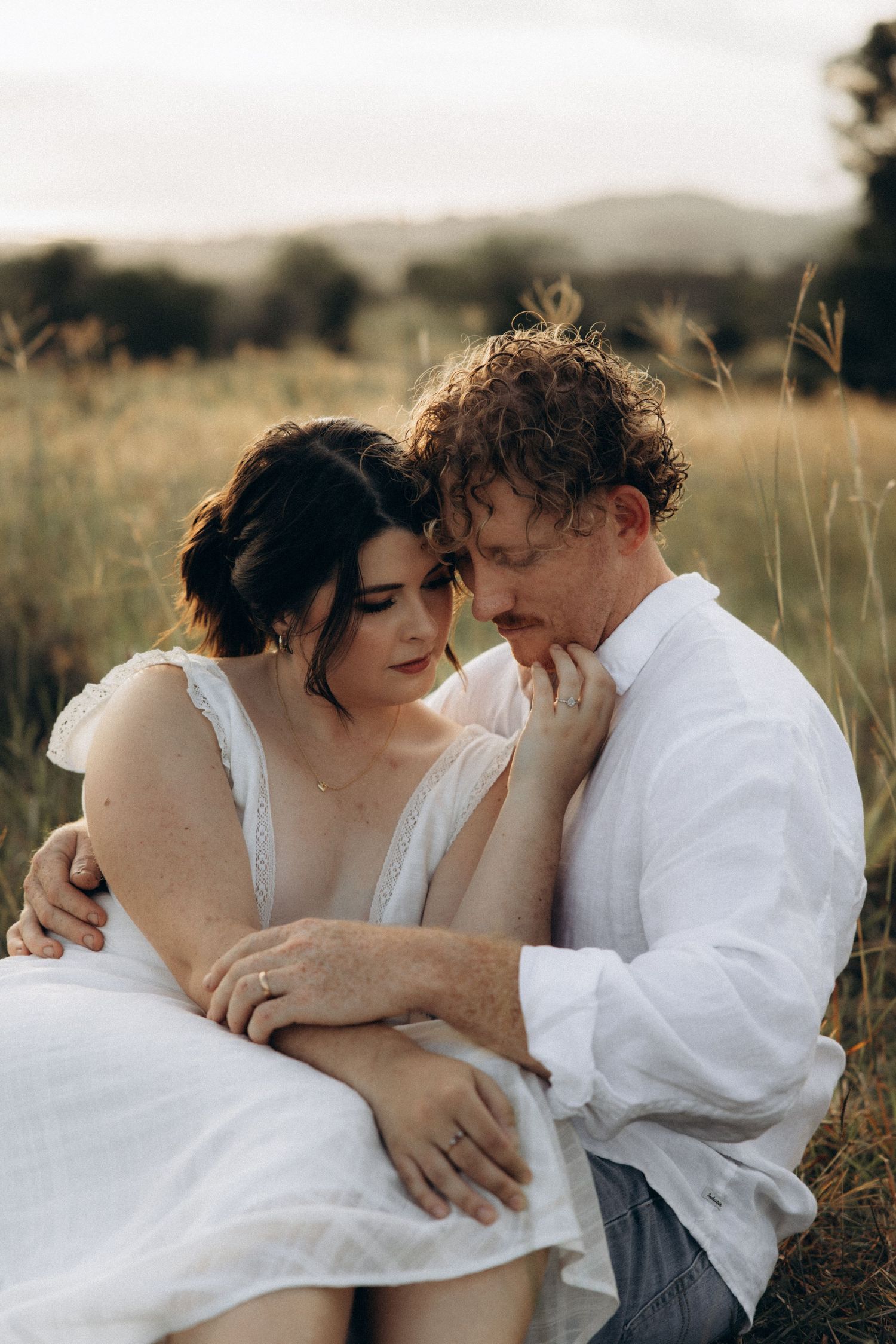 Romantic couple embraces in golden hour light among tall grass.