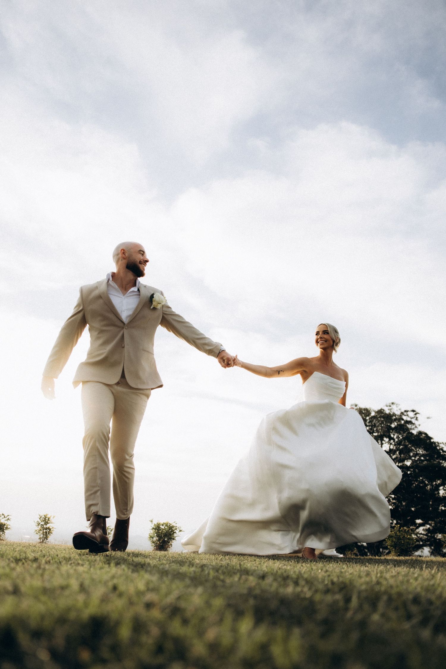 Playful wedding couple dancing and twirling on a hilltop at sunset.