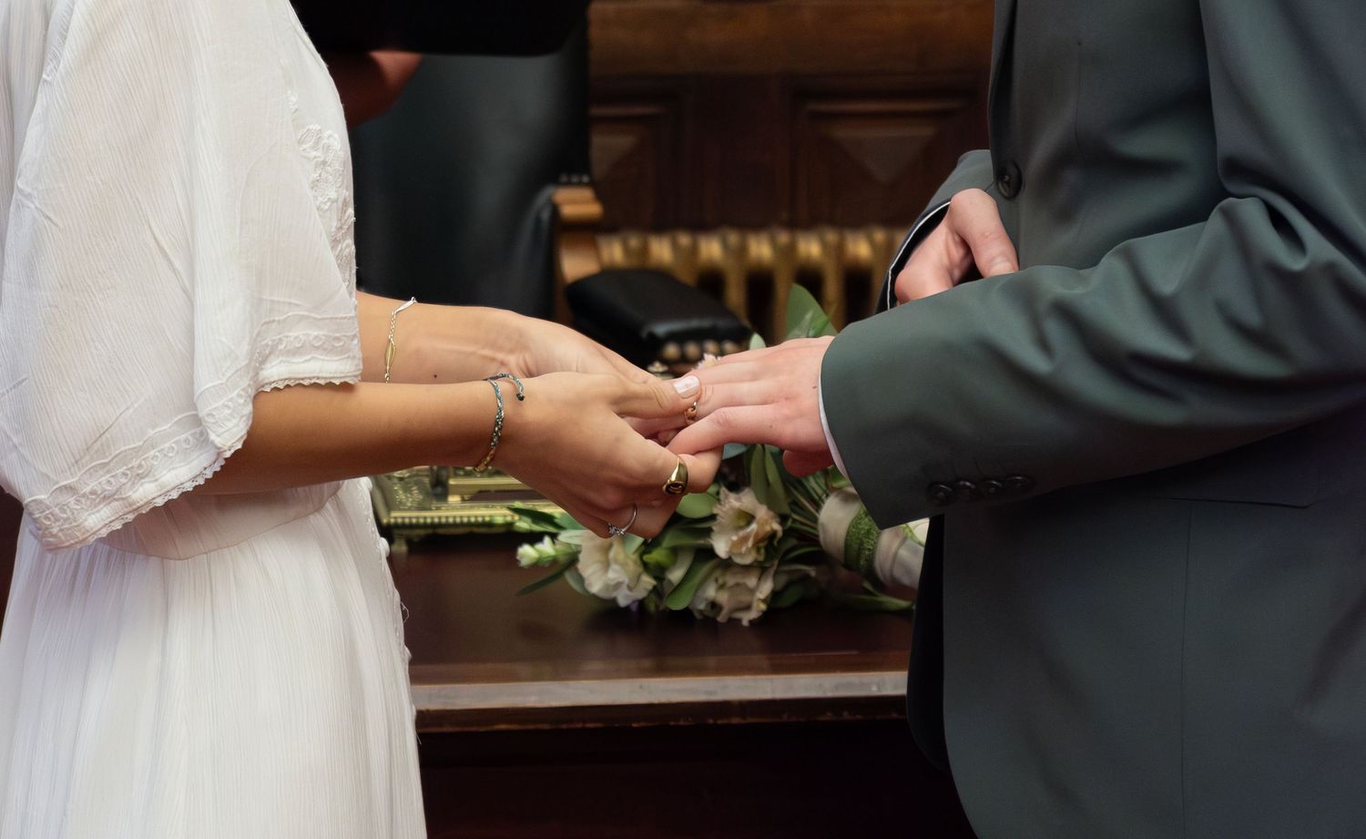 Close-up of a bride and groom exchanging wedding rings during a ceremony, a bouquet in the background.