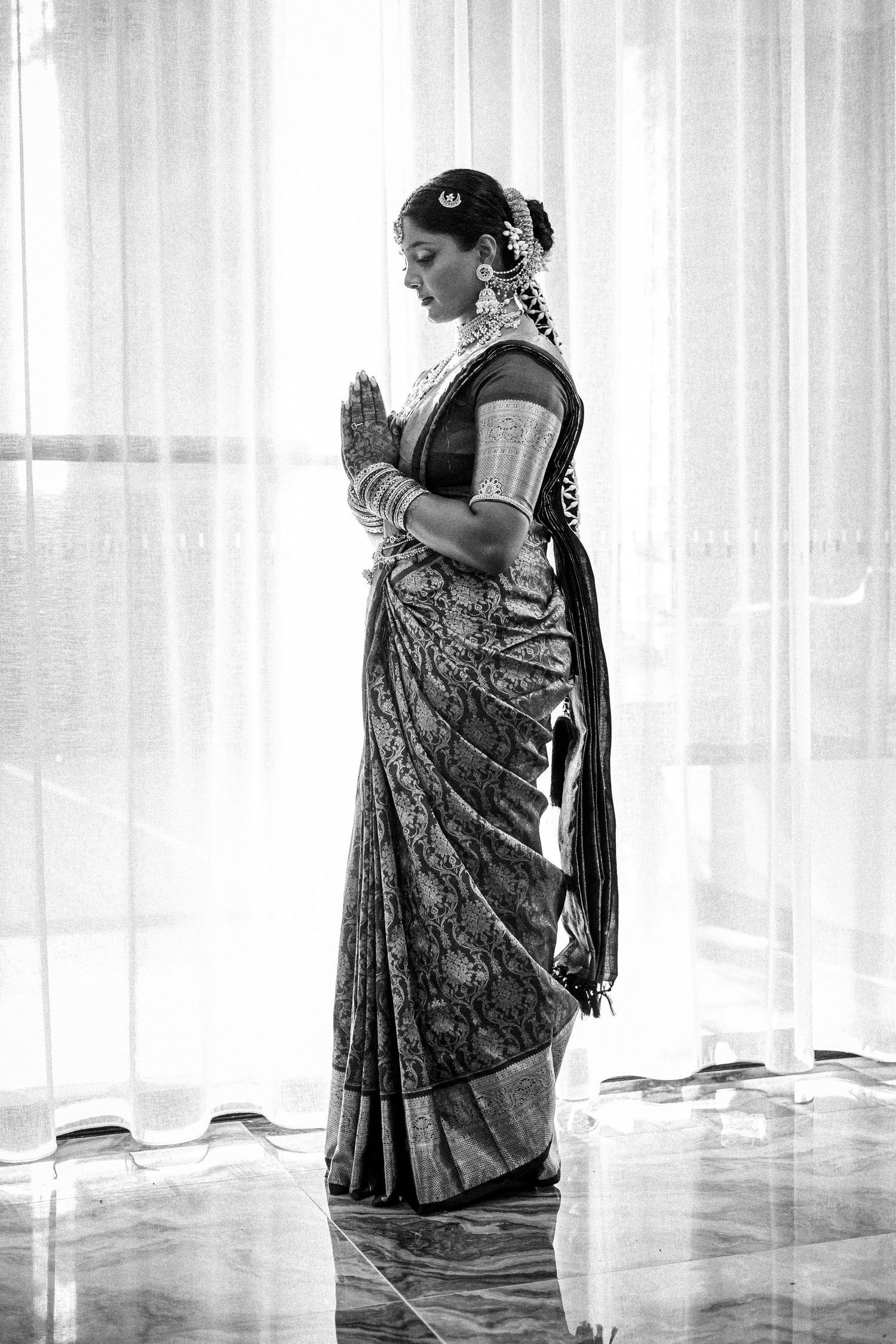 Indian bride in a silk saree with hands in prayer pose in black and white.