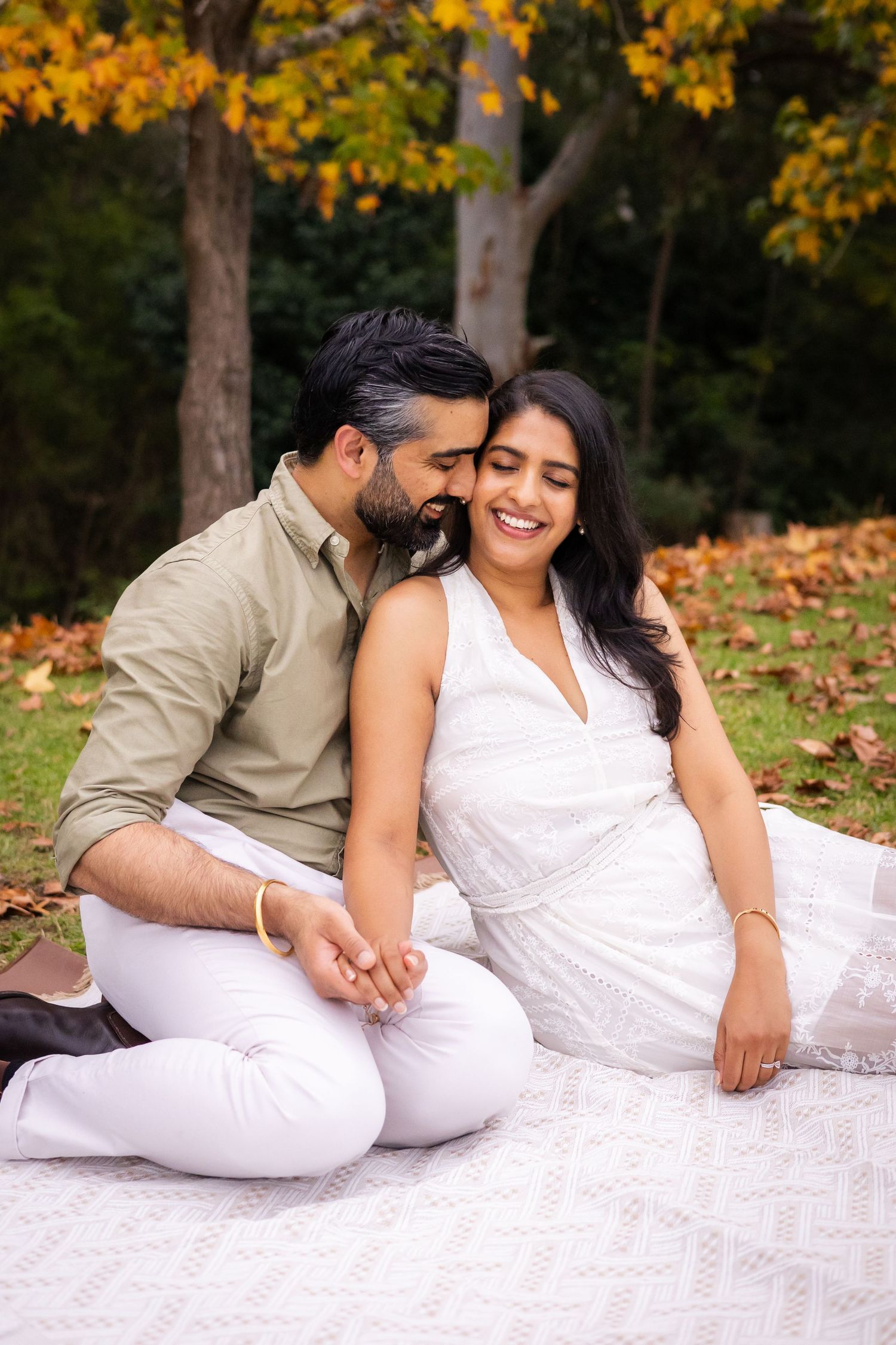 Couple sharing a romantic moment on a blanket surrounded by autumn foliage.