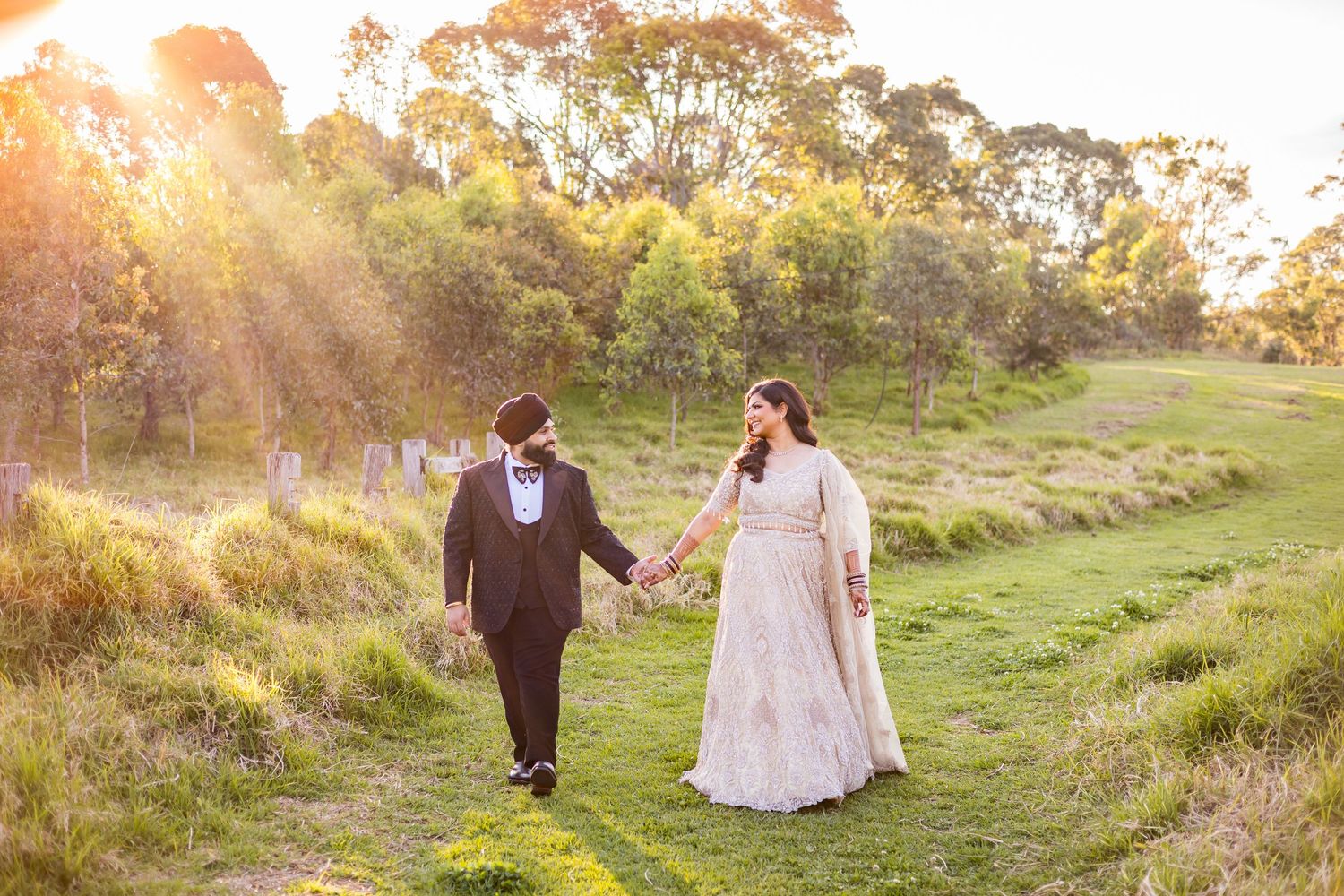 Couple holding hands walking through a sunlit green meadow at golden hour.