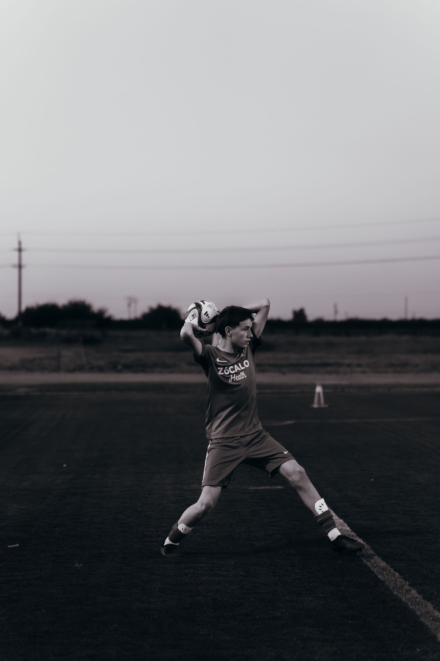 Soccer player in dark uniform practices dramatic shot technique on field at dusk with athletic form.