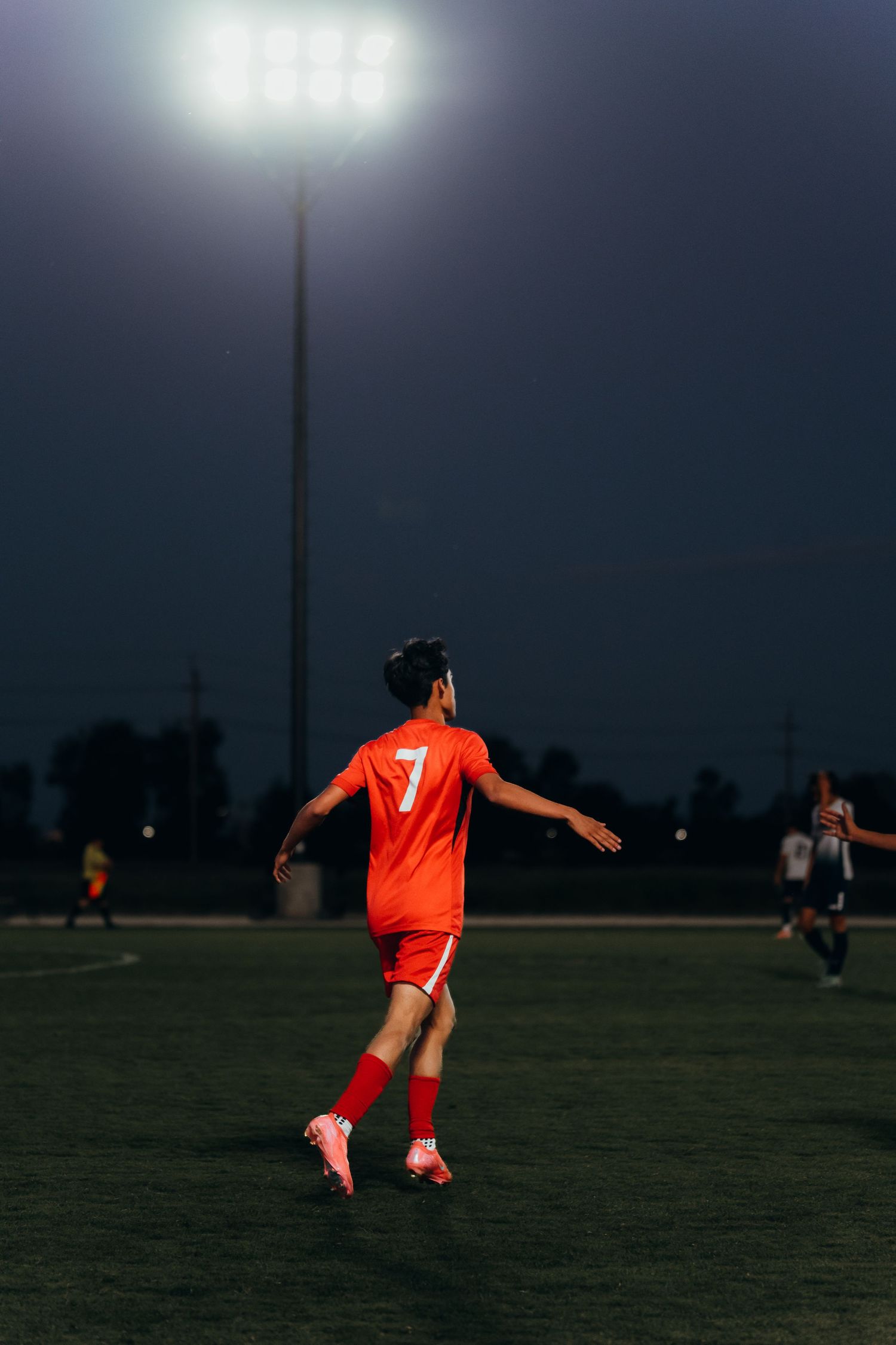 Soccer player in orange jersey number 7 running on illuminated field at night under bright stadium lights.