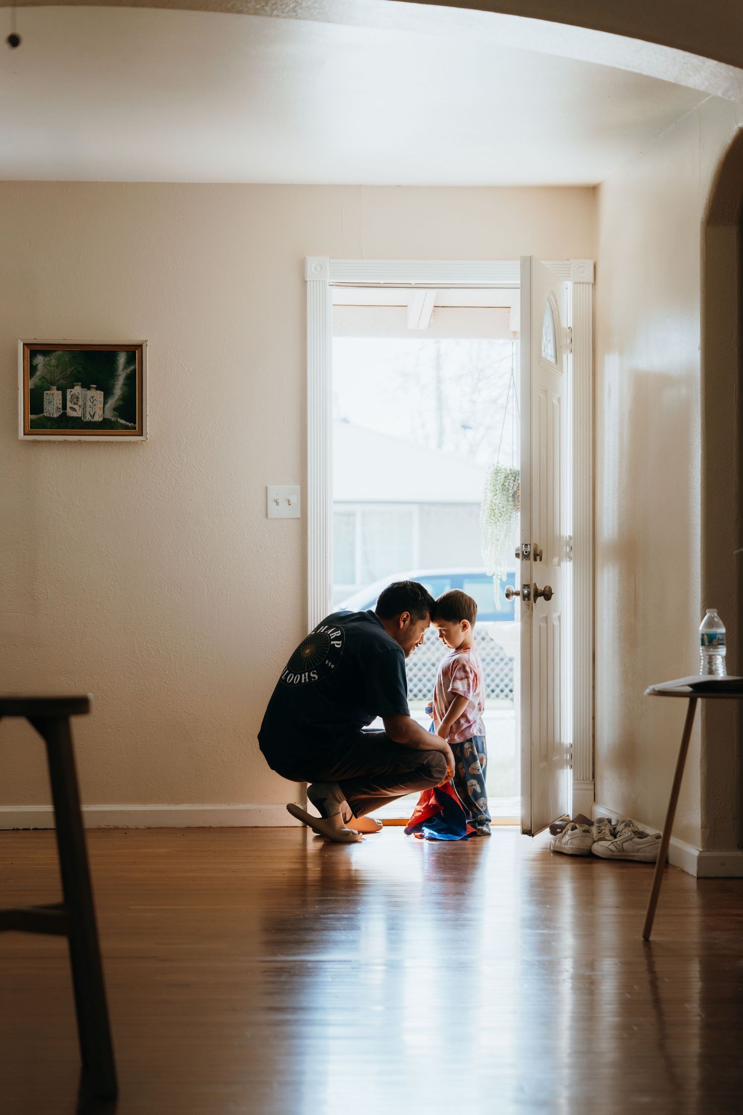 Adult helping child with shoes near front door of home with hardwood floors.